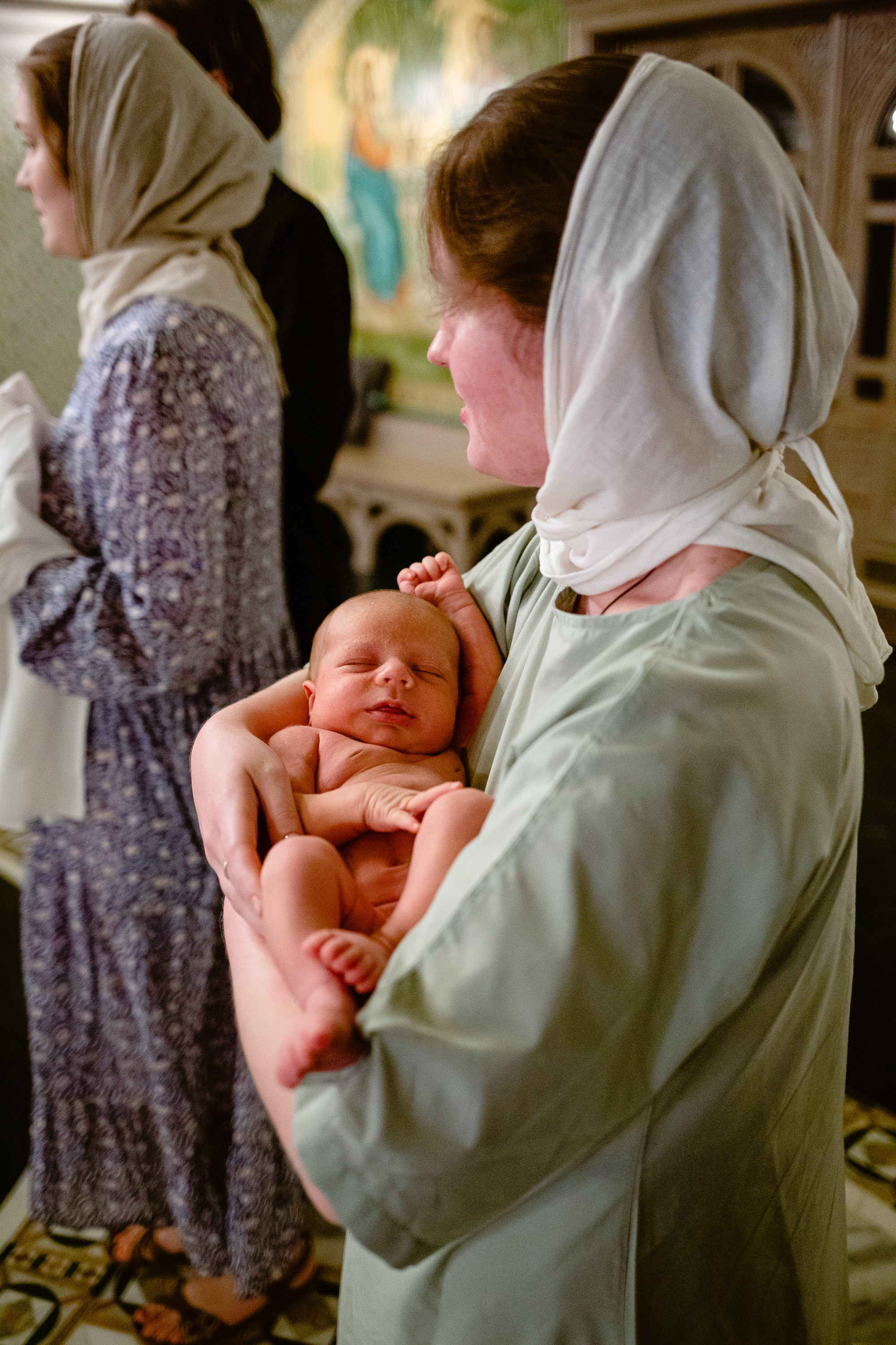 Фотосъемка крещения в сретенском монастыре. Крестная держит на руках младенца, который будет креститься.