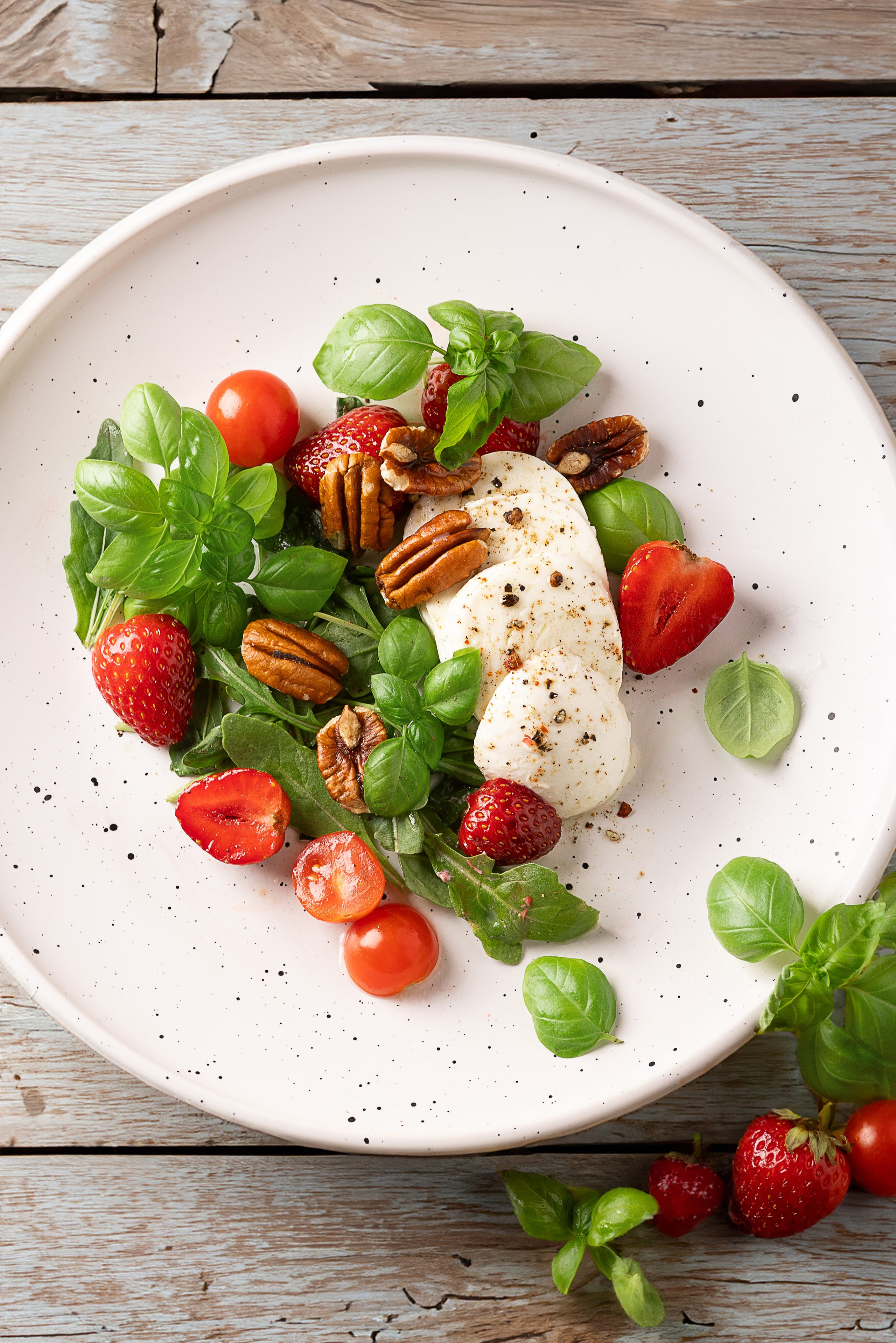 Салат из черри, моцареллы и клубники с базиликом с соусом песто. Салат Капрезе на деревянном фоне