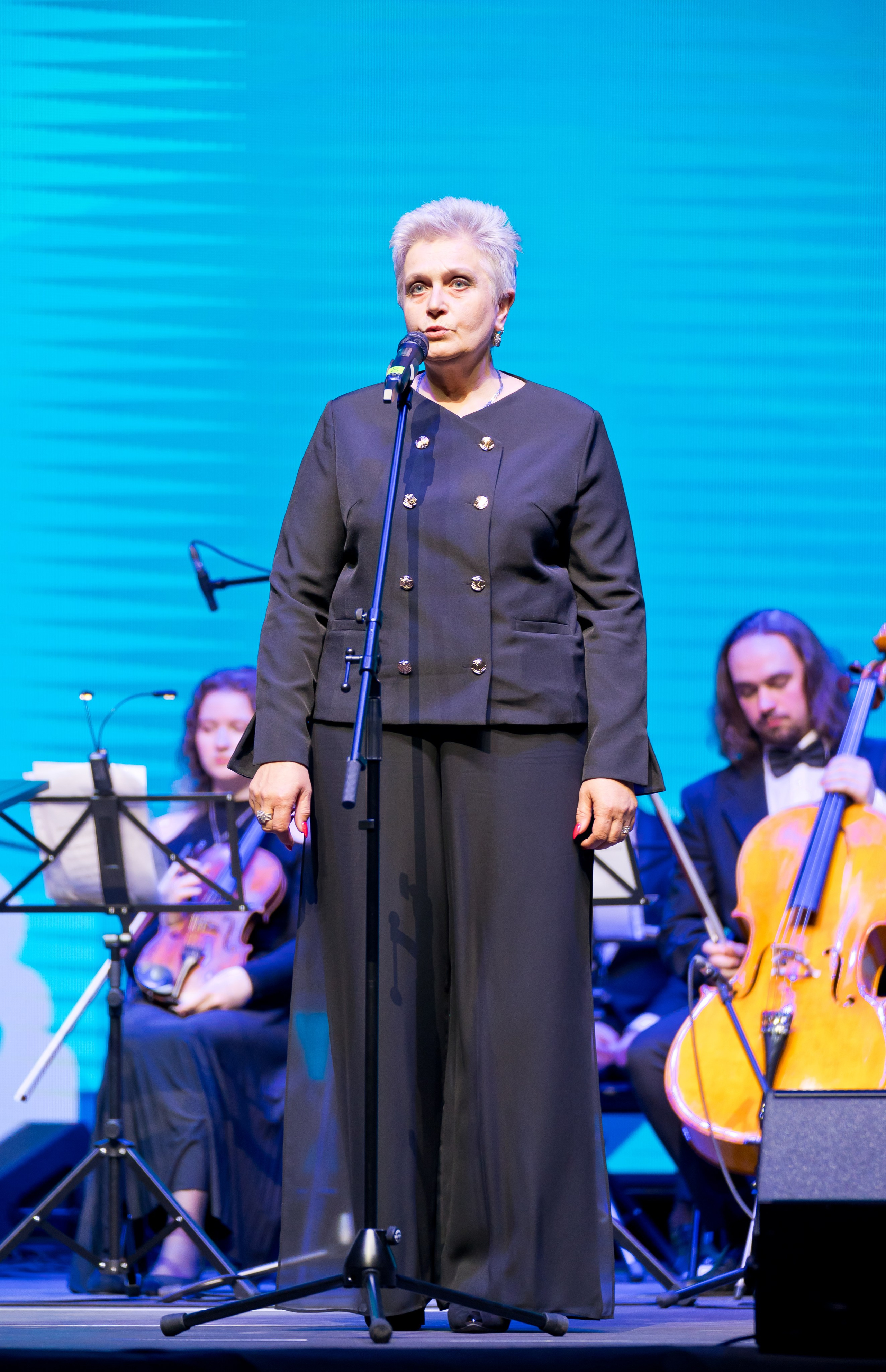 Женщина с короткими седыми волосами выступает у микрофона на сцене. Церемония Дня местного самоуправления в Санкт-Петербурге | Фото: Евгений Мальцев.