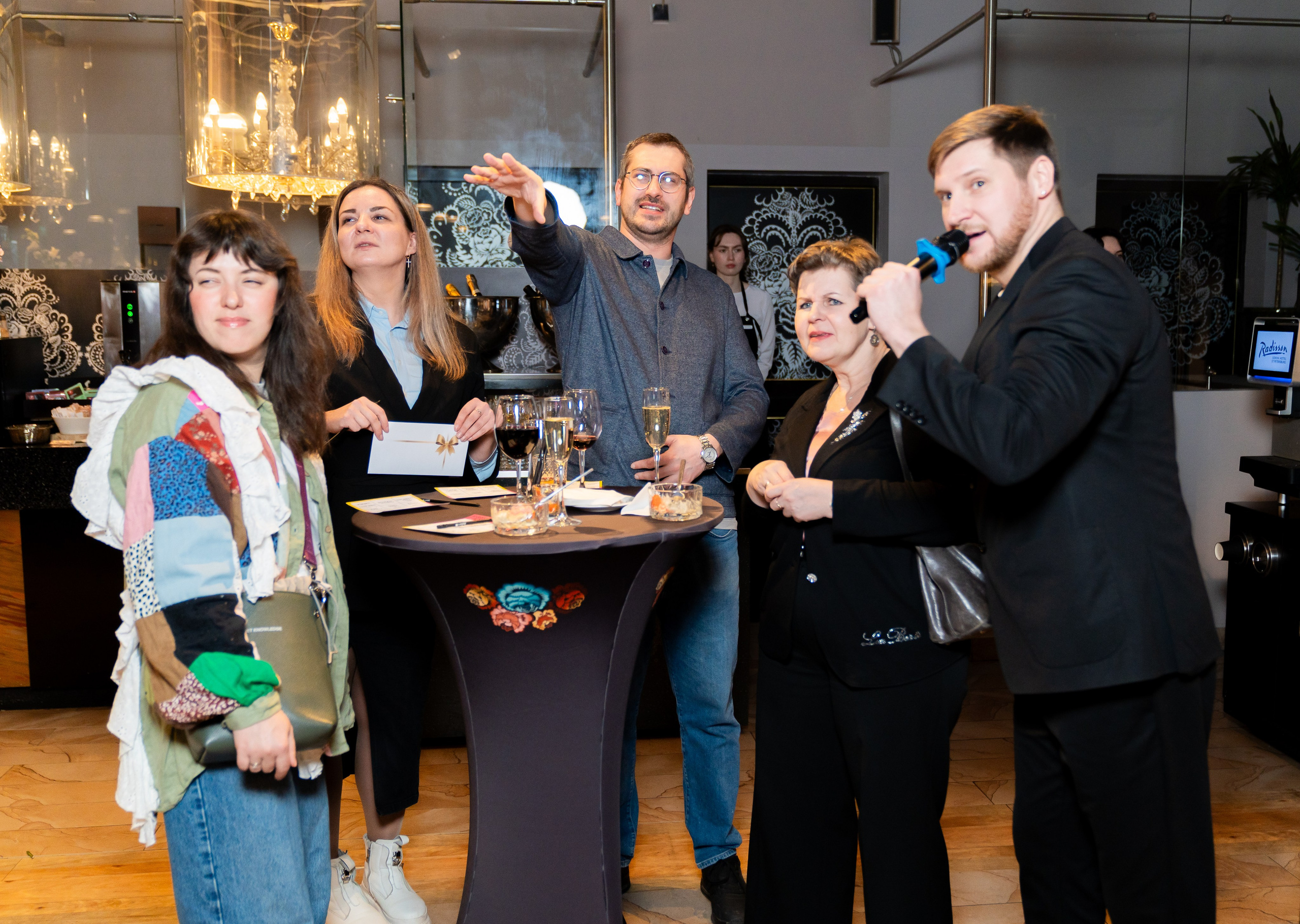 Ведущий с микрофоном и участники розыгрыша у стола на корпоративе в Radisson Sonya. Фотограф Евгений Мальцев.