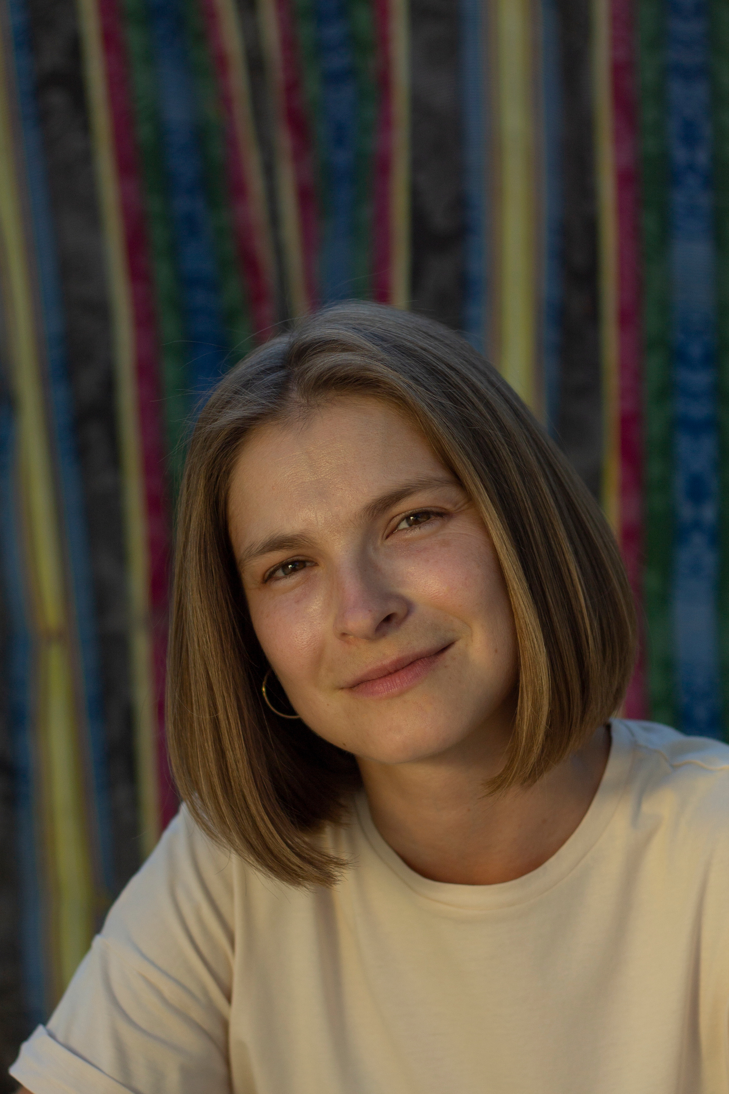 Девушка в светлой футболке на фоне полосатого матраса улыбается в камеру