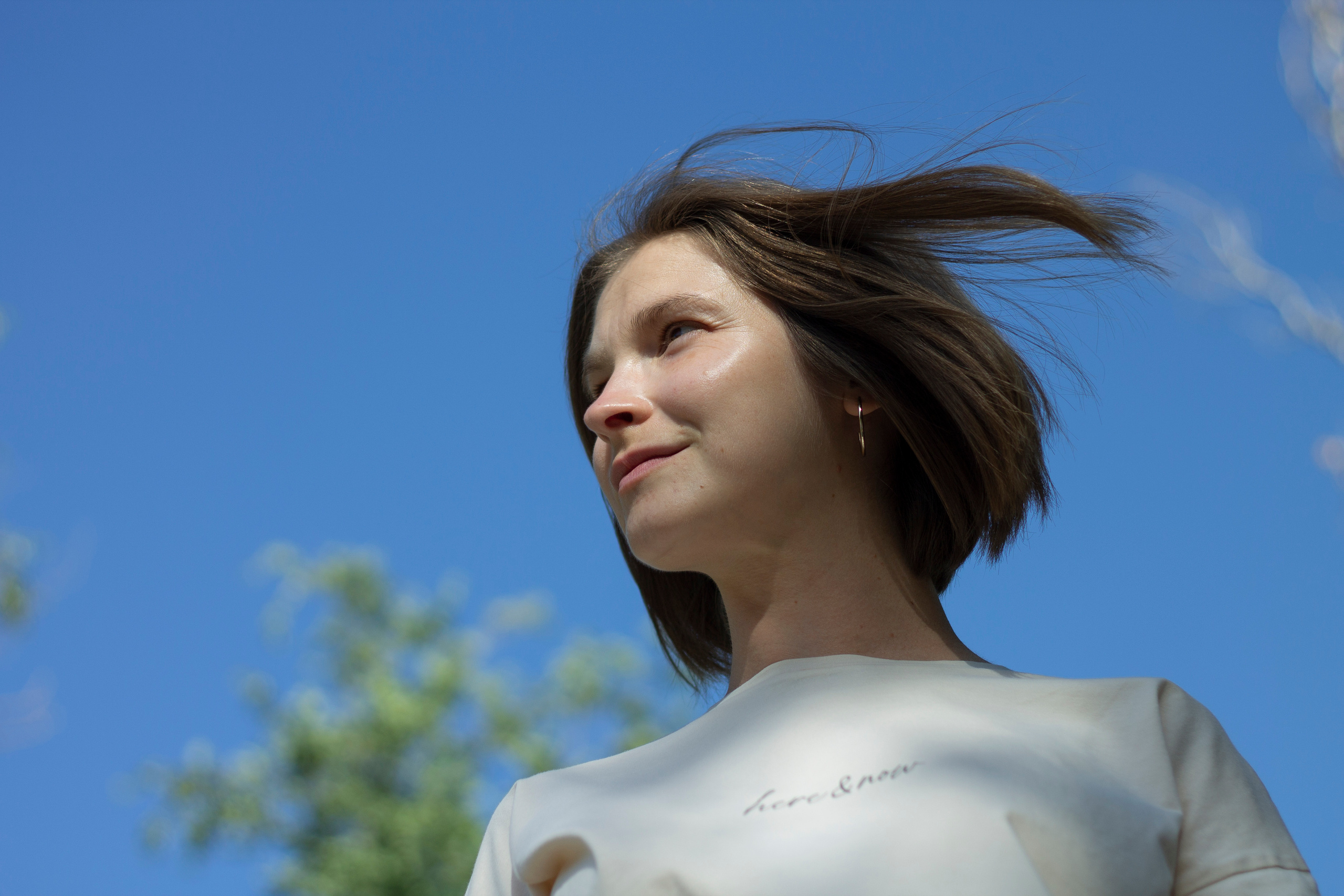 Ветер развевает волосы девушки в бежевой футболке на фоне голубого неба