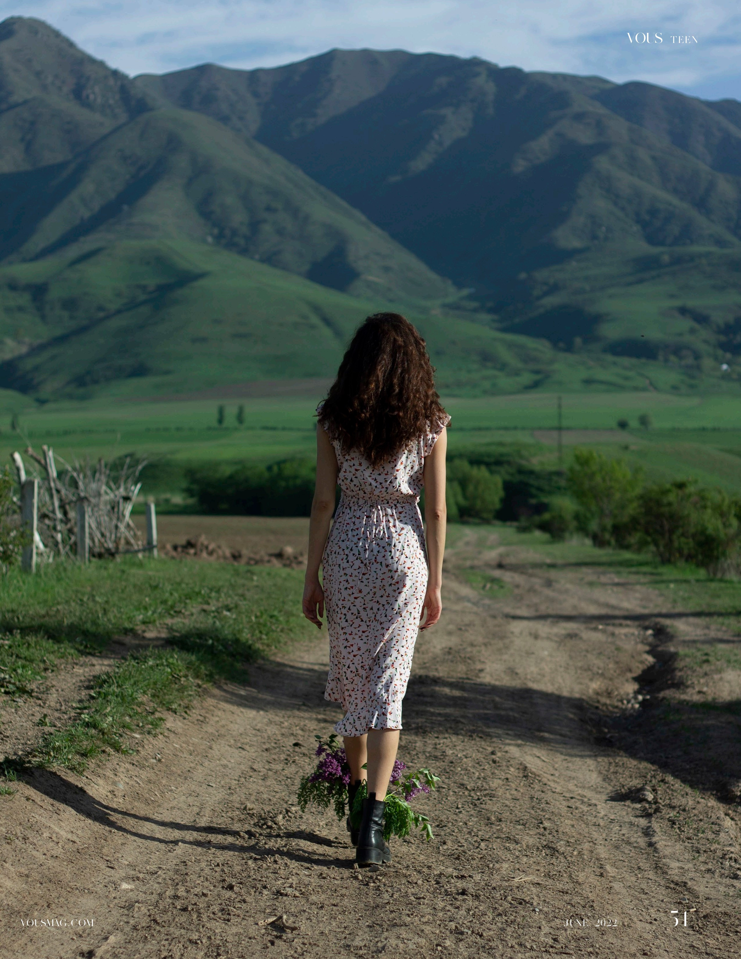 Девушка в платье по проселочной дороге уходит в горы 