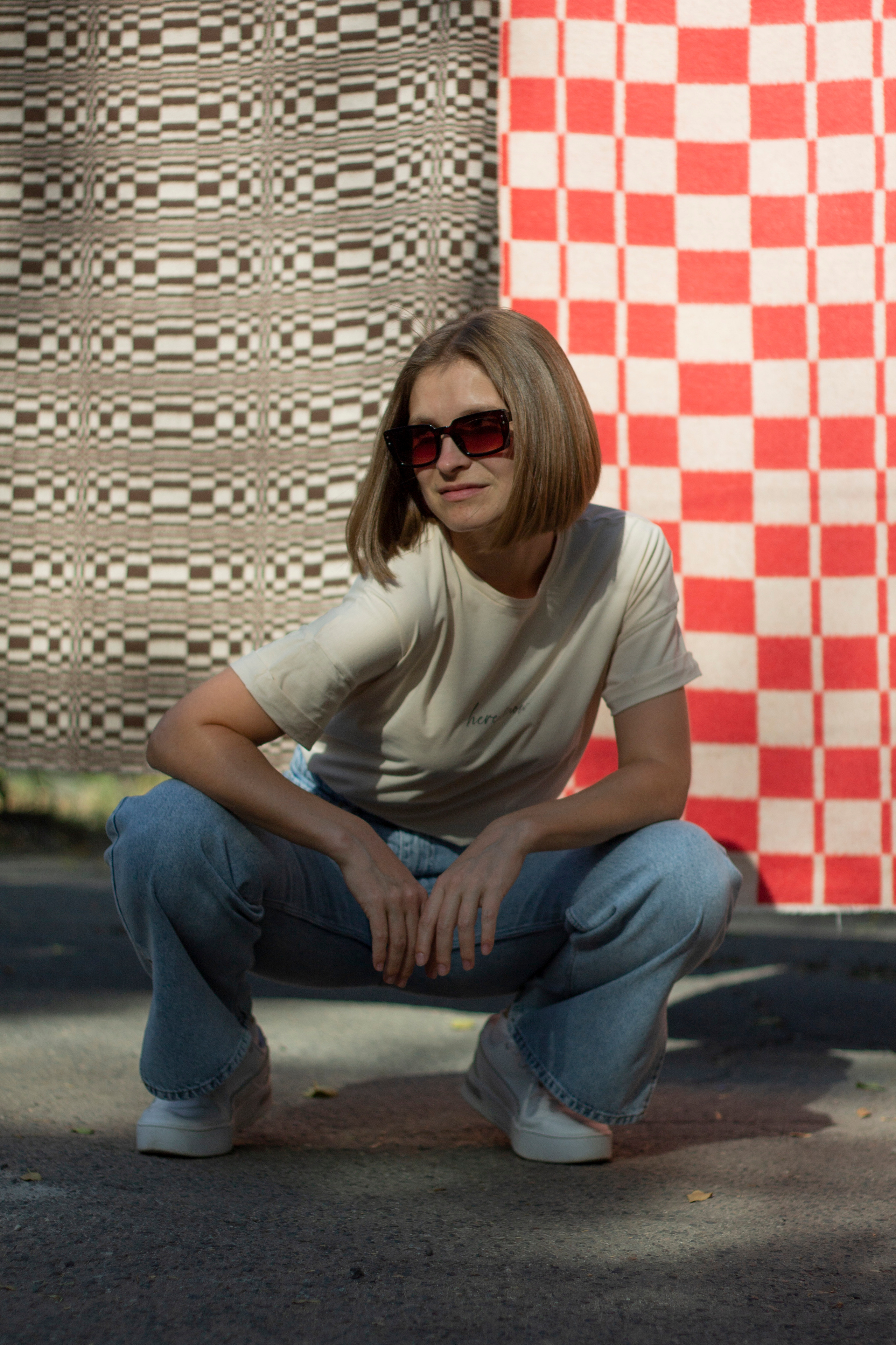 Девушка в джинсах сидит на корточках между двух пледов красного и серого