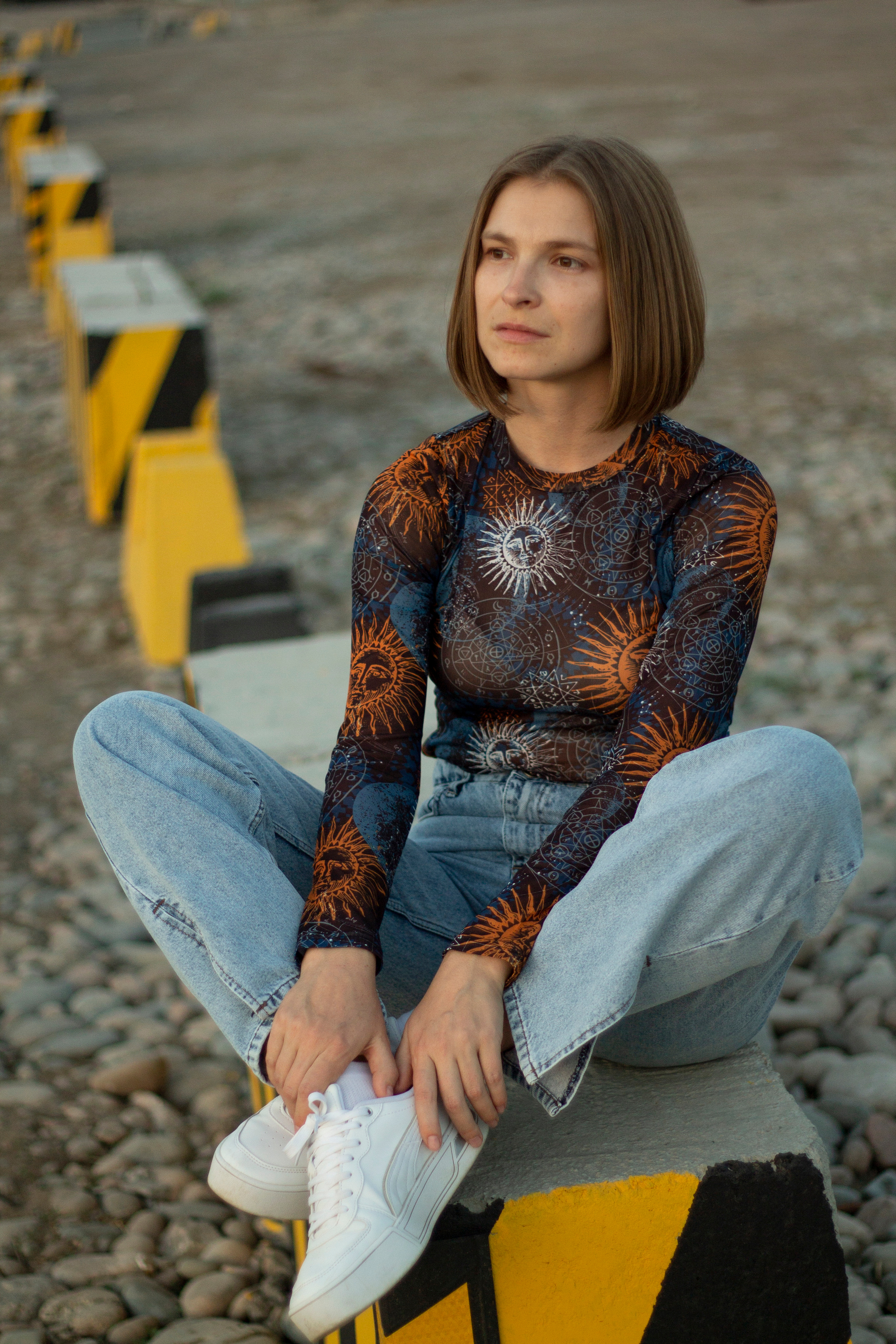 Девушка сидит на бетонном блоке поджав ноги смотрит вдаль