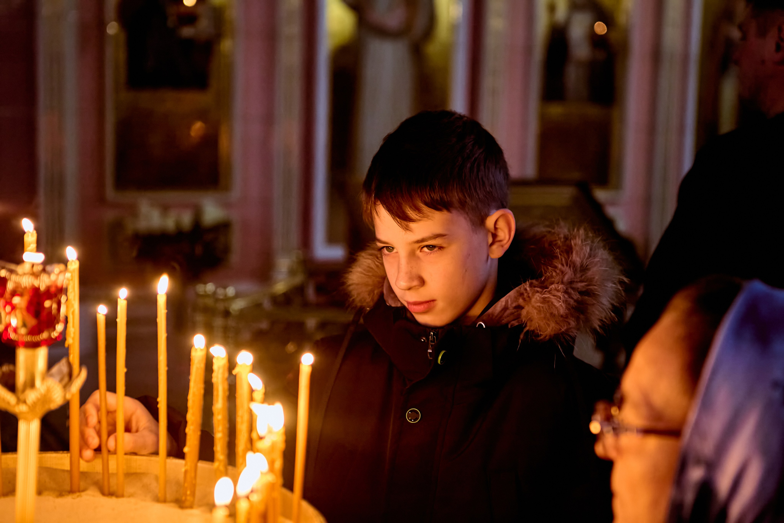 У праздничного подсвечника стоит мальчик 13 лет и возжигает свечу о здравии