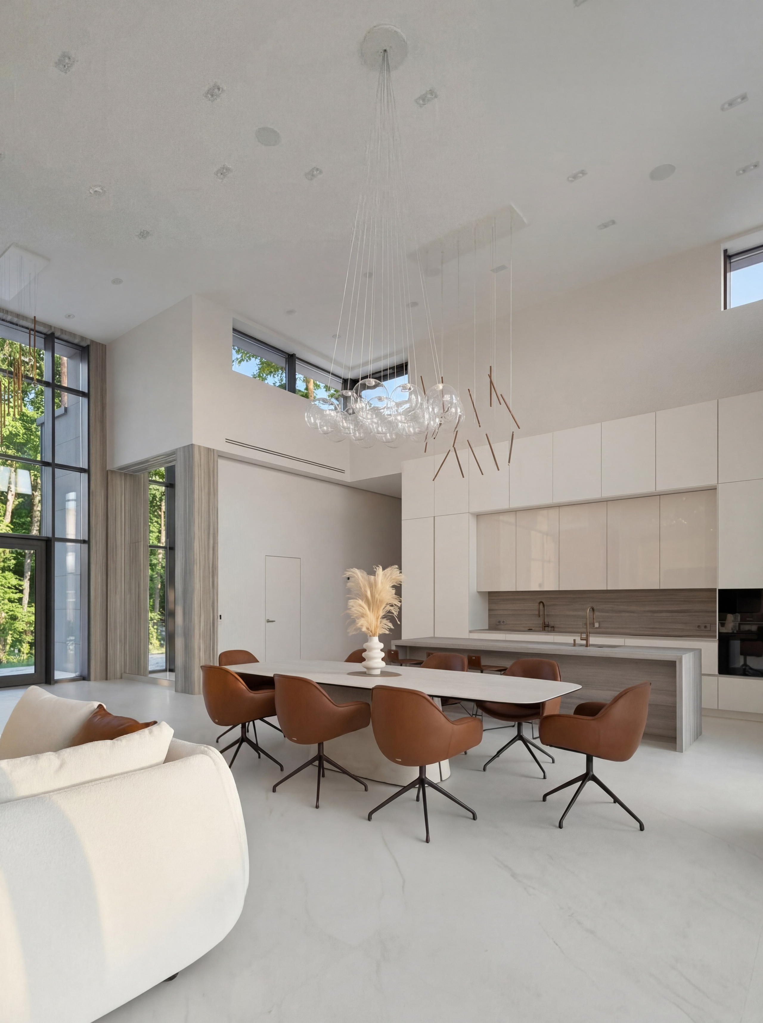 Интерьер кухни-столовой от Валерии Котович в доме у воды: минималистичная белая кухня с островом, длинный обеденный стол с терракотовыми креслами и дизайнерская стеклянная люстра в двухсветном пространстве.