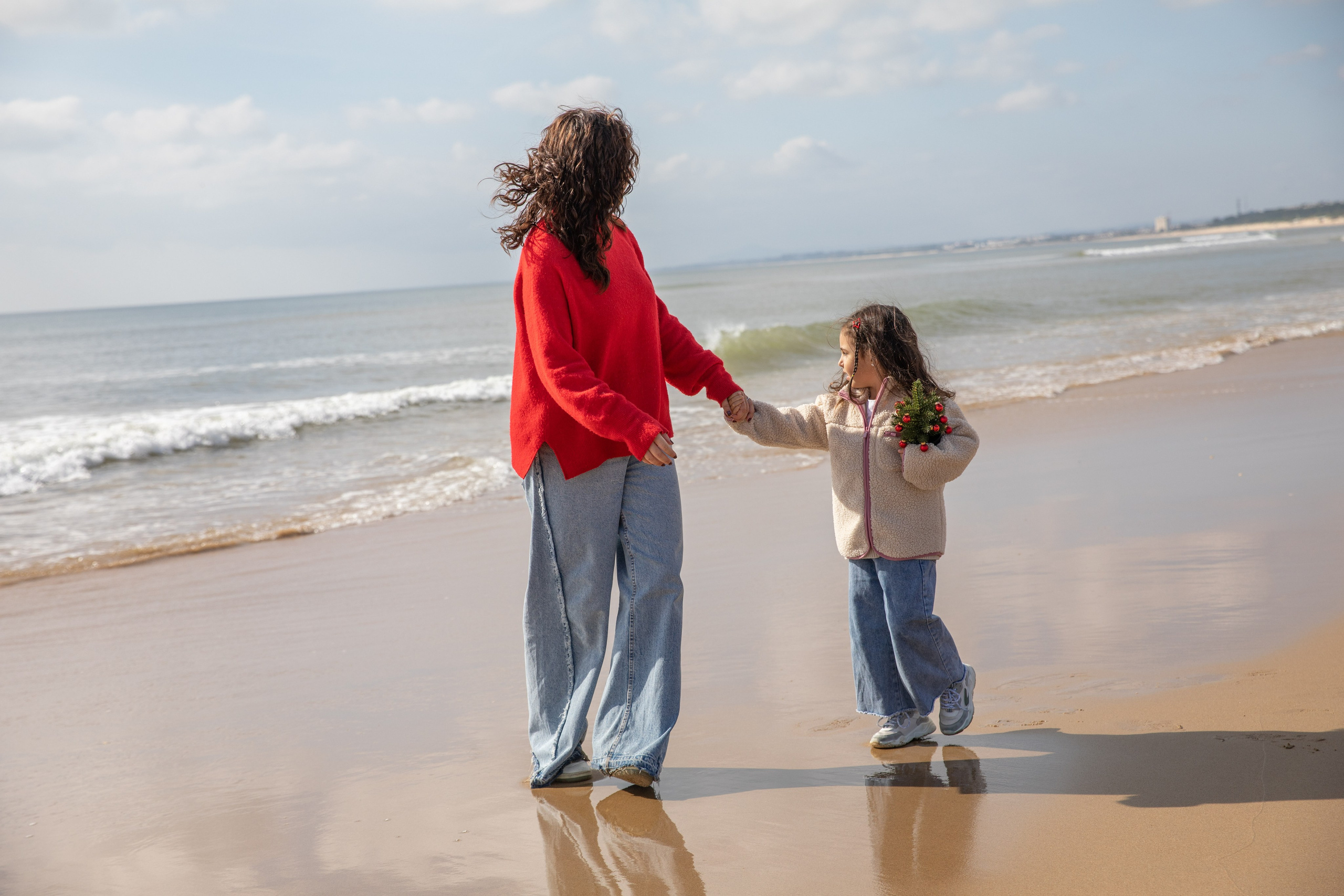 Mum, dad, and daughter laughing together as the waves touch their feet. Mum and daughter walking hand in hand, enjoying a peaceful stroll along the beach