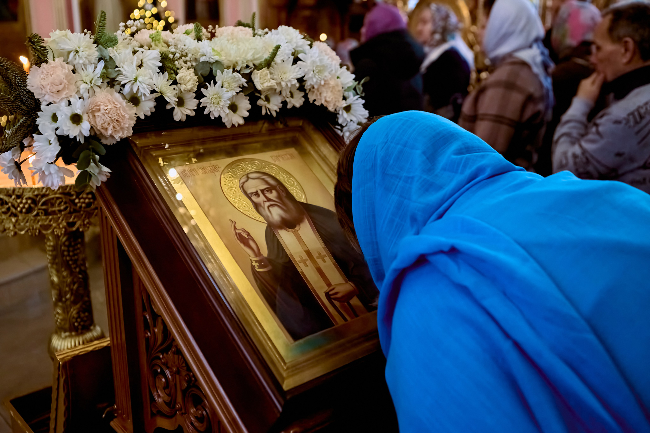 Женщина в сине-голубом платке склонилась пред иконой Преподобного Серафима Саровского