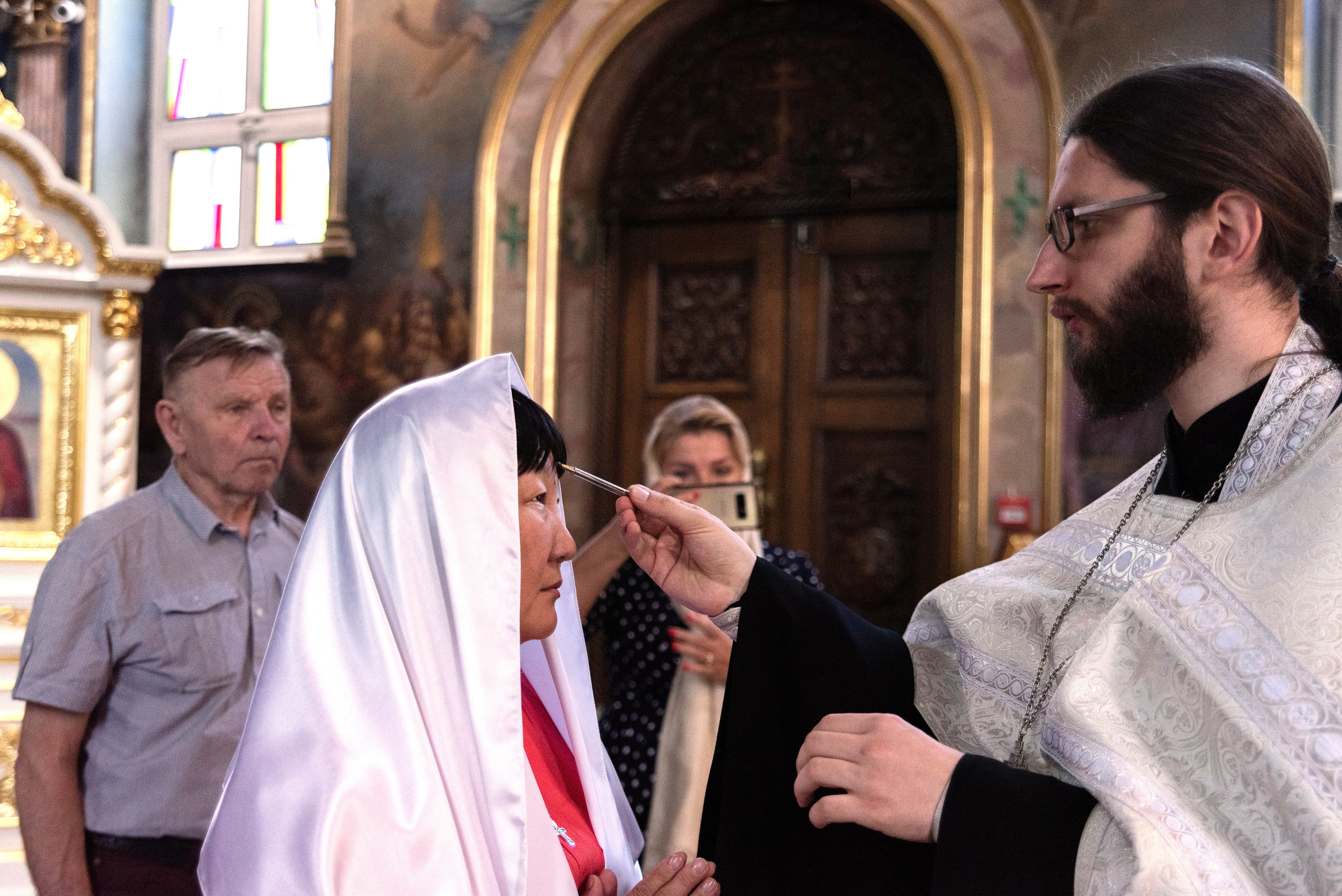 Священник мажет елеем голову женщины на крещении в храме Краснодара