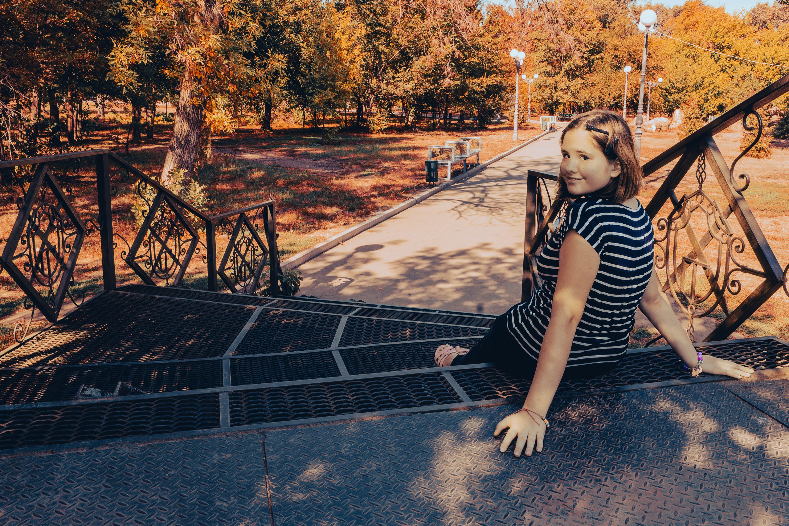 Девочка сидит вполоборота на мосту и смотрит в объектив через плечо