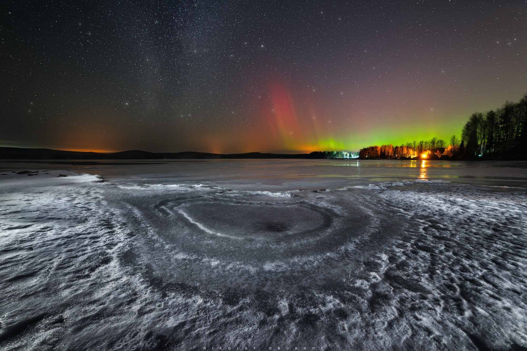 Весенний лед на озере ночью во время полярного сияния на Урале. Ночной пейзаж со звездами и сиянием