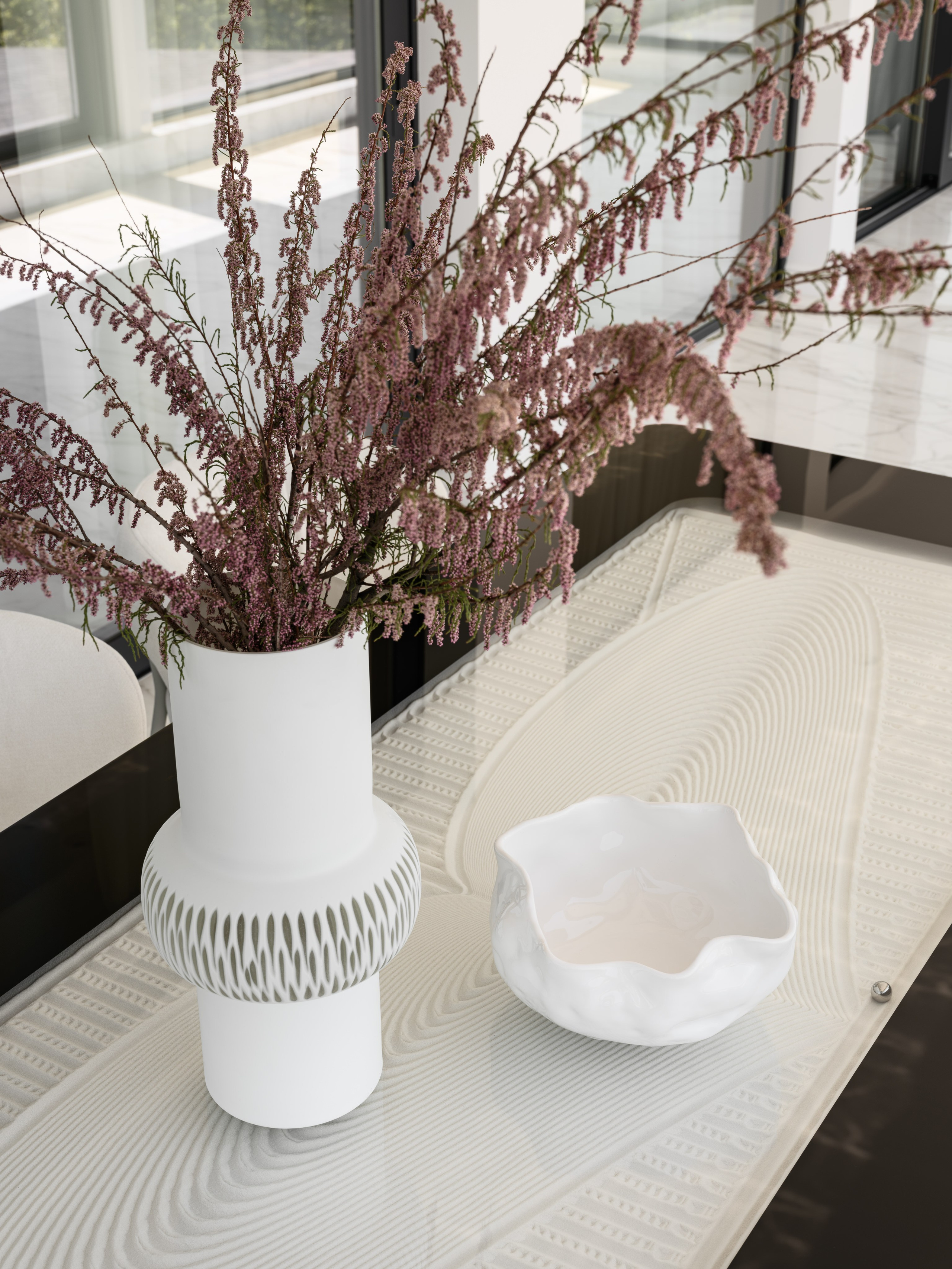 Крупный план декоративной композиции на стеклянном столе в современной столовой: белая ваза с ветвями вереска и керамическая чаша на фактурной поверхности. Элегантный декор от Алёны Боярской, стилист Наталья Якушева, фотограф Сергей Денисенко.