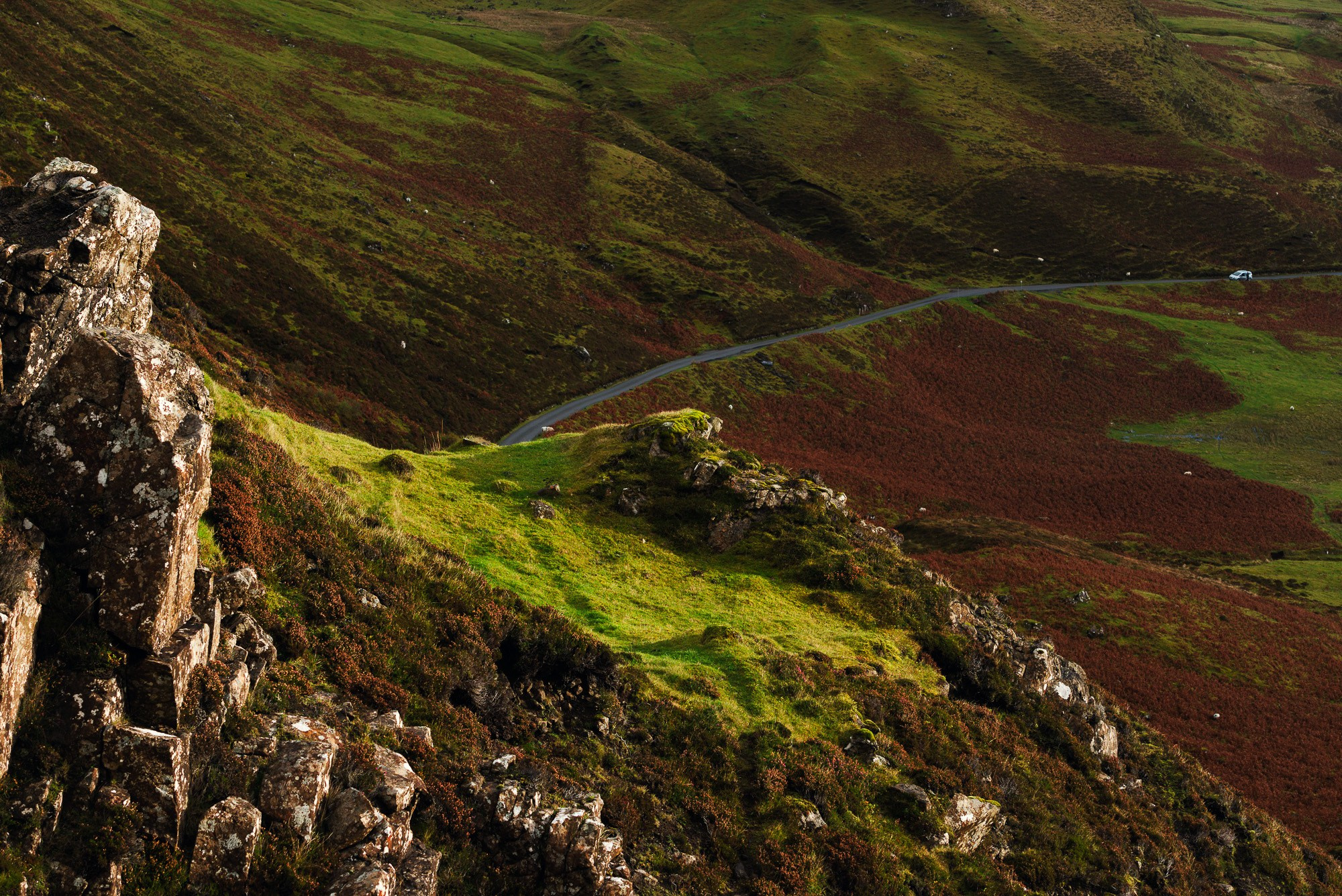 Вид на извилистую дорогу в горном ландшафте Куиранг на острове Скай, Шотландия, с зелеными и коричневыми холмами