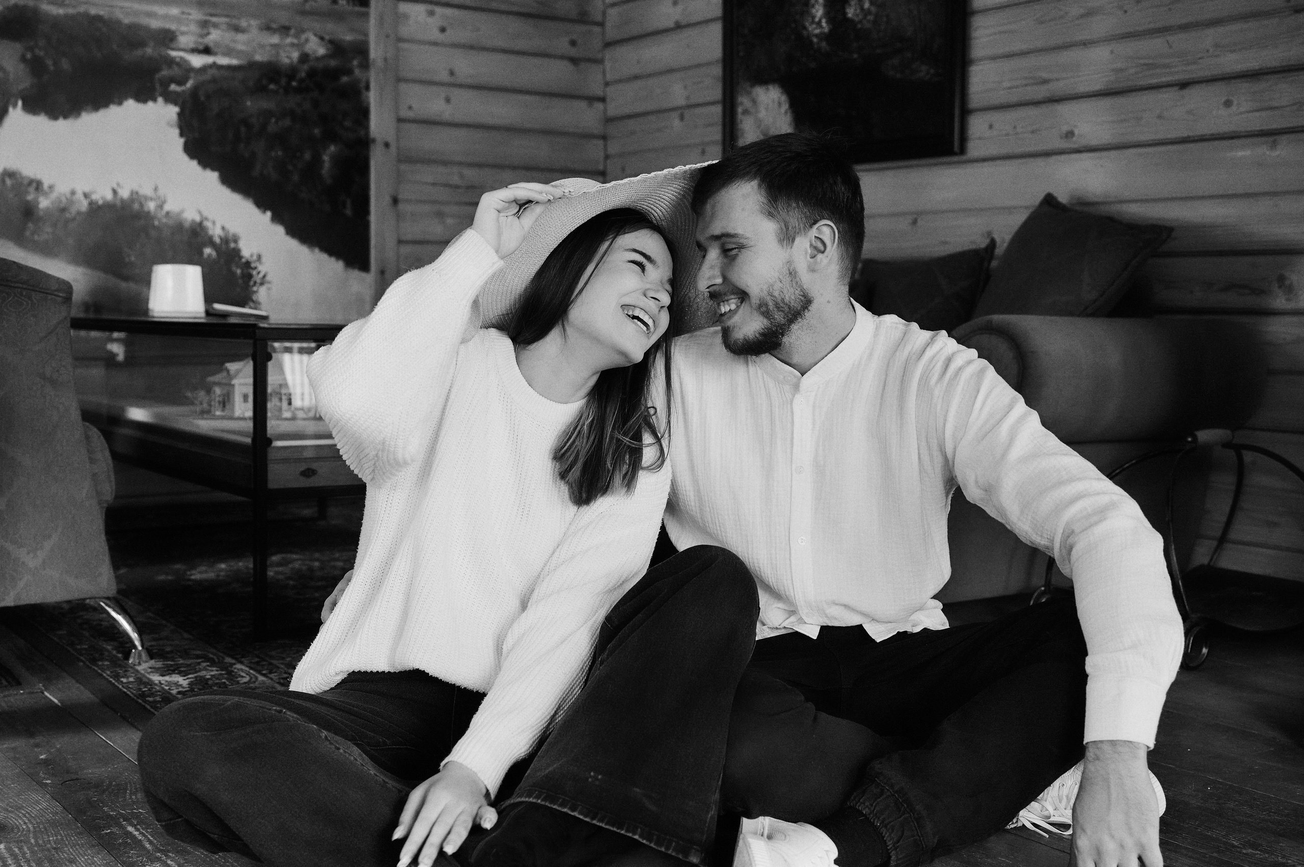 Родители сидят на полу, смеются и смотрят друг на друга — чёрно-белая фотография.