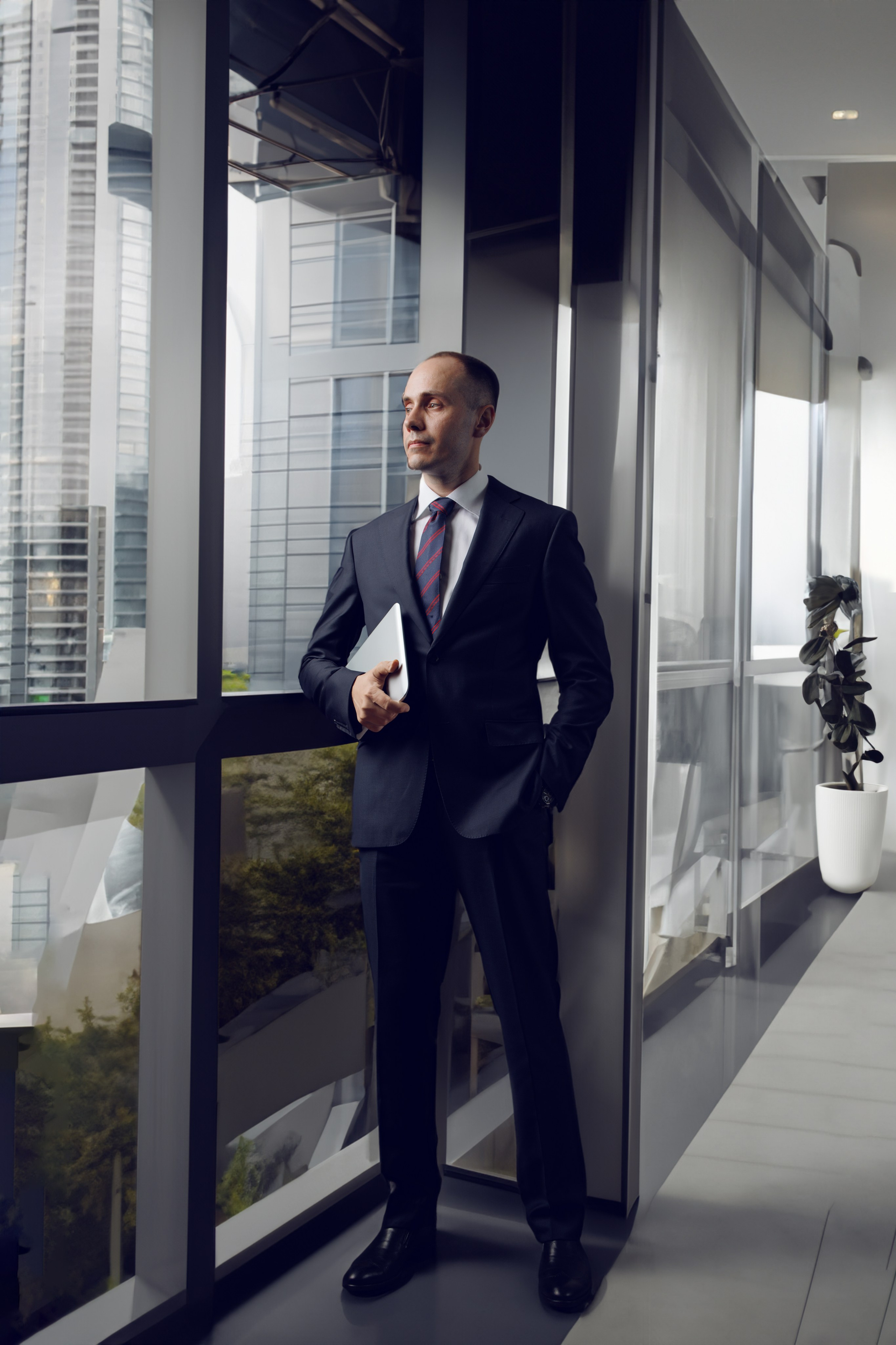Мужчина в деловой одежде стоит во весь рост в просторном офисе.