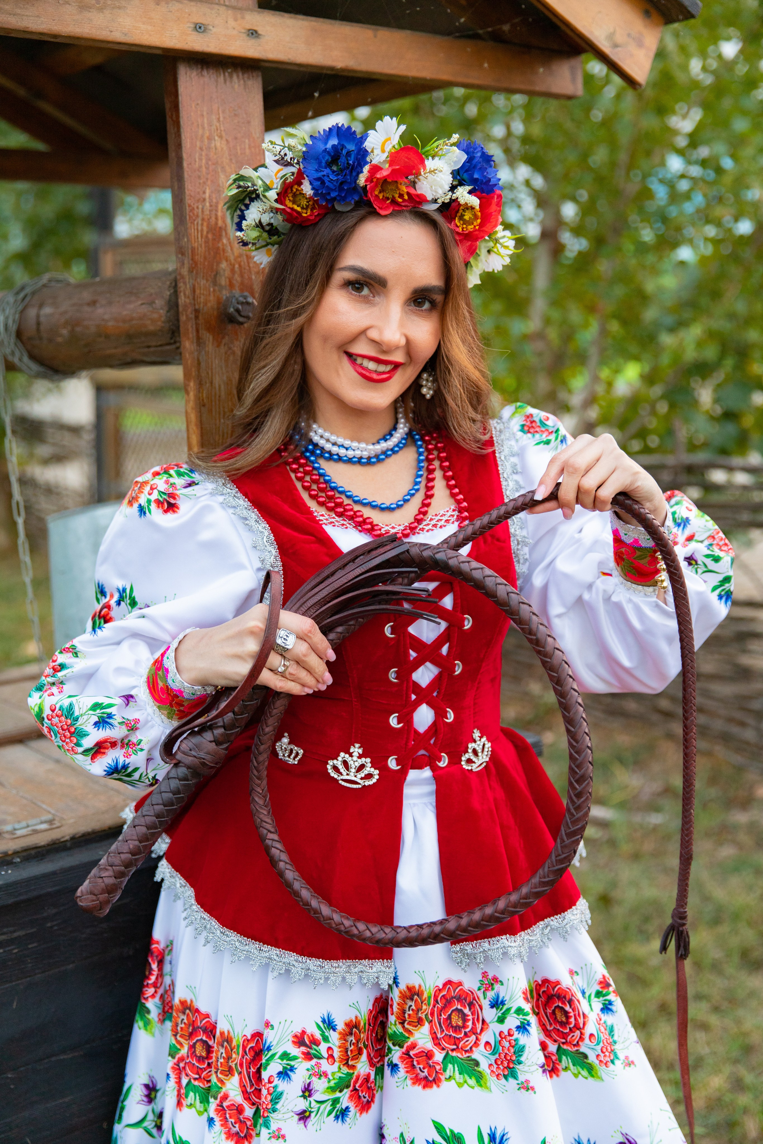 Красивая девушка в казачке с плеткой в руках передаёт дух стремления и свободы, находясь на фоне живописного пейзажа.