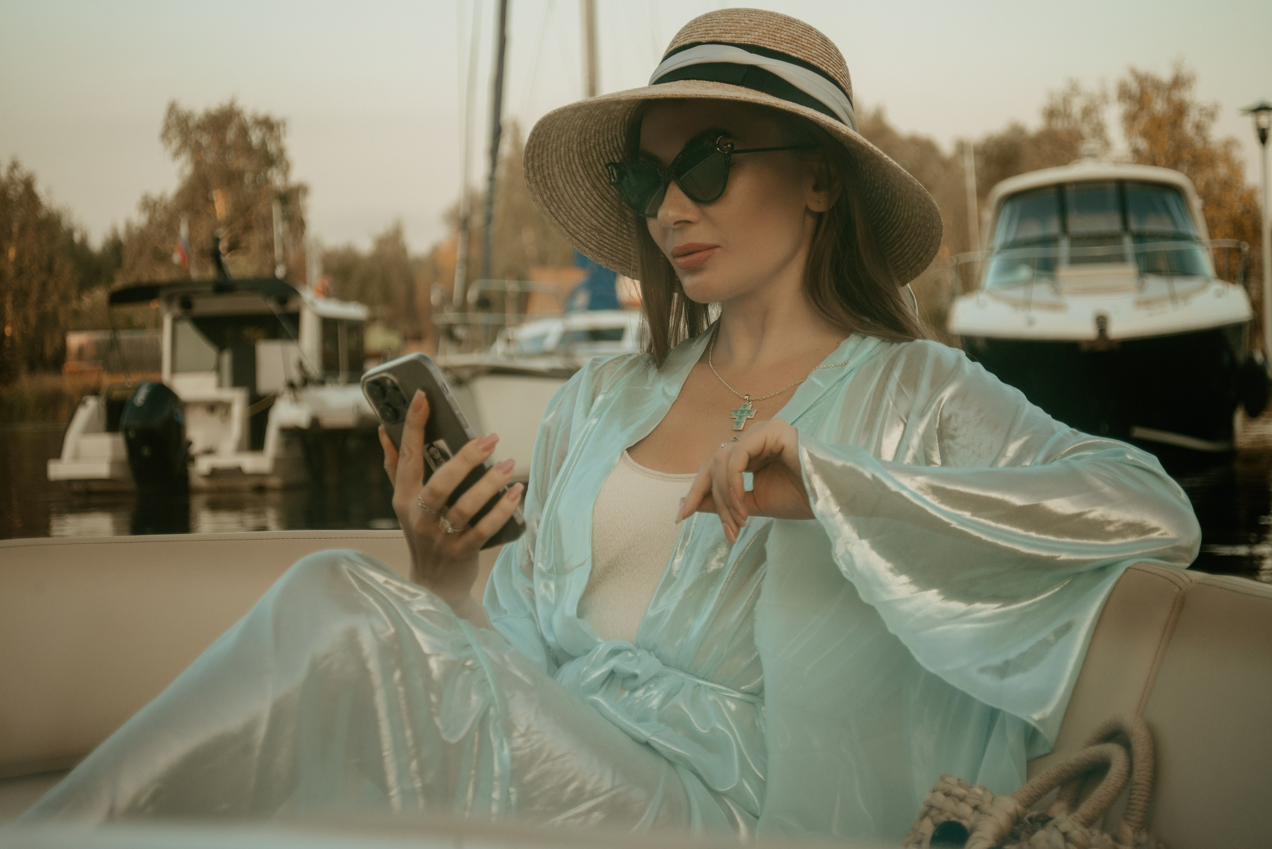 Фотосессия в стиле олд мани дамы в широкополой шляпе и темных очках с телефоном на фоне яхт