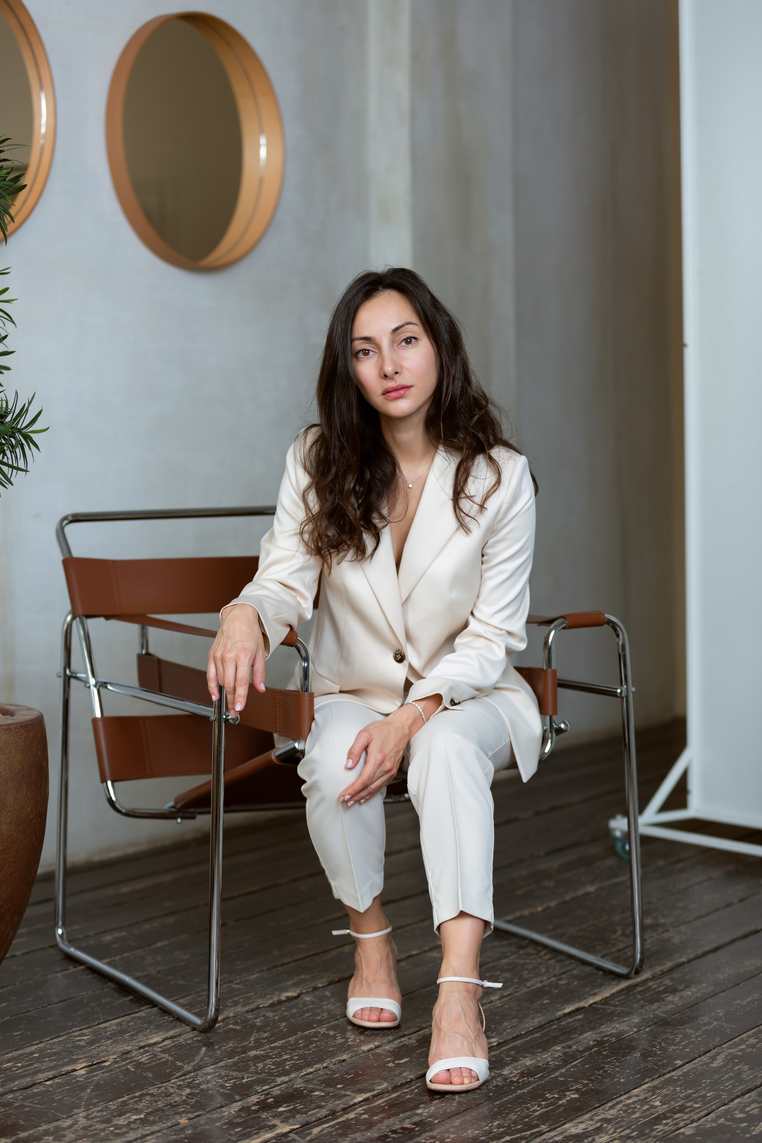 Стильная фотосессия в светлой студии — модель в белом костюме сидит на стуле.