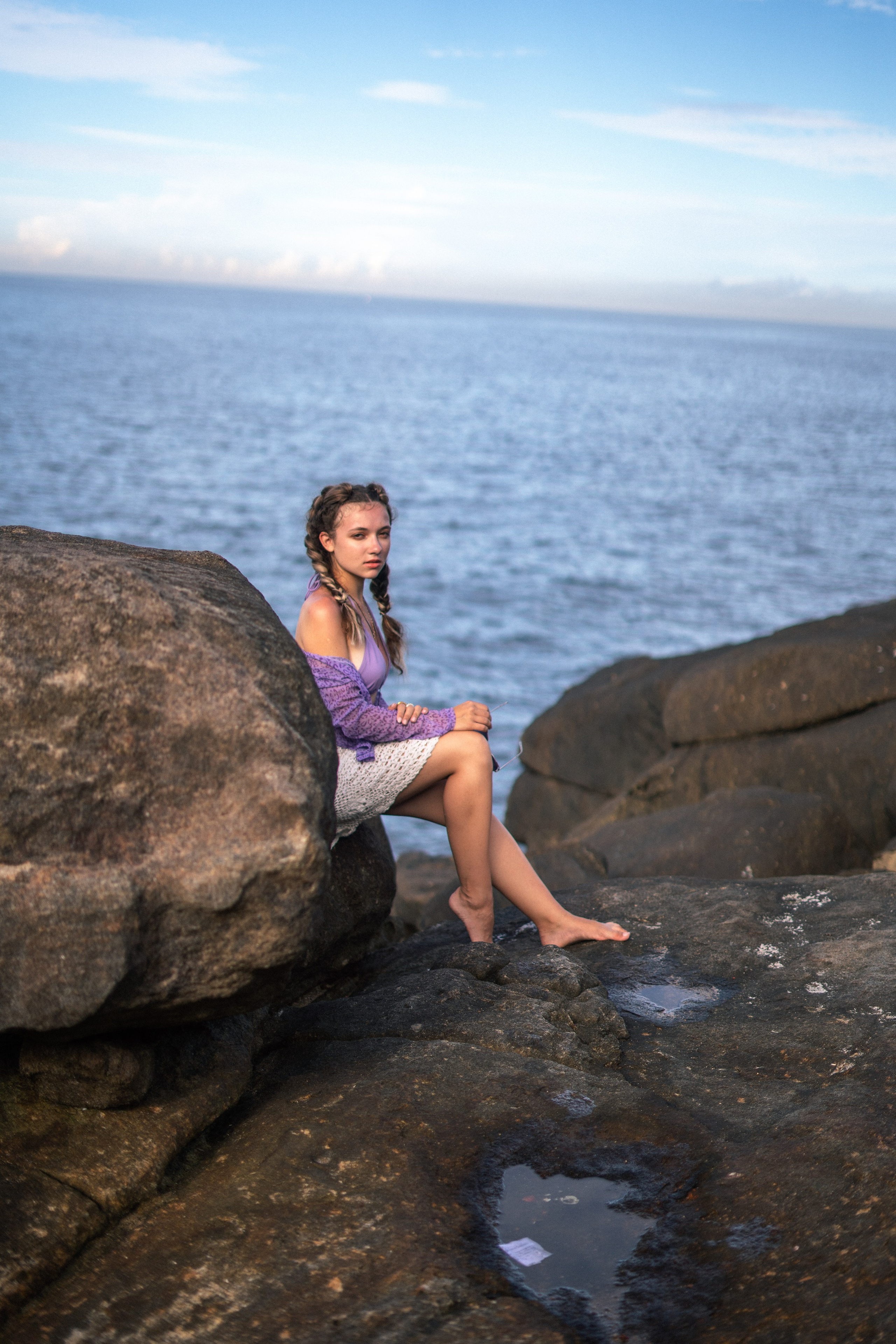 a girl in a purple swimsuit playing with water by the rocks