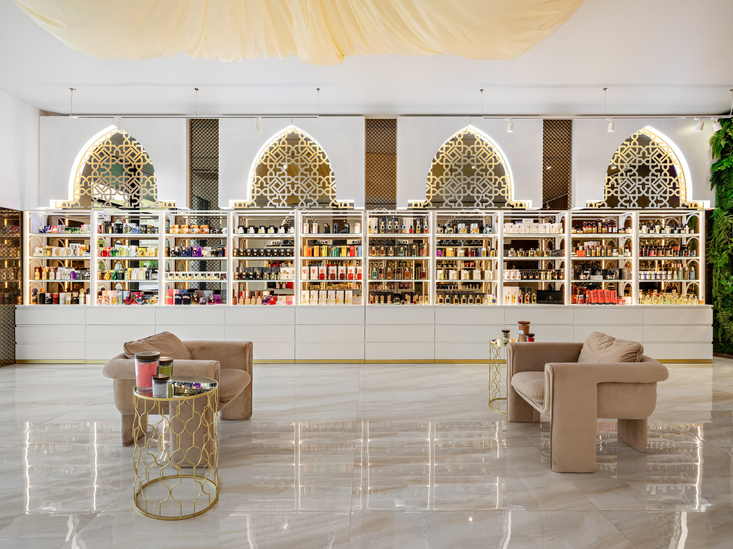 Современный интерьер парфюмерного бутика с золотыми арками, белыми стеллажами, подсветкой и коллекцией премиальных духов. Зона отдыха с креслами и столиками, дизайнер Мария Никишина, фотограф Сергей Денисенко.