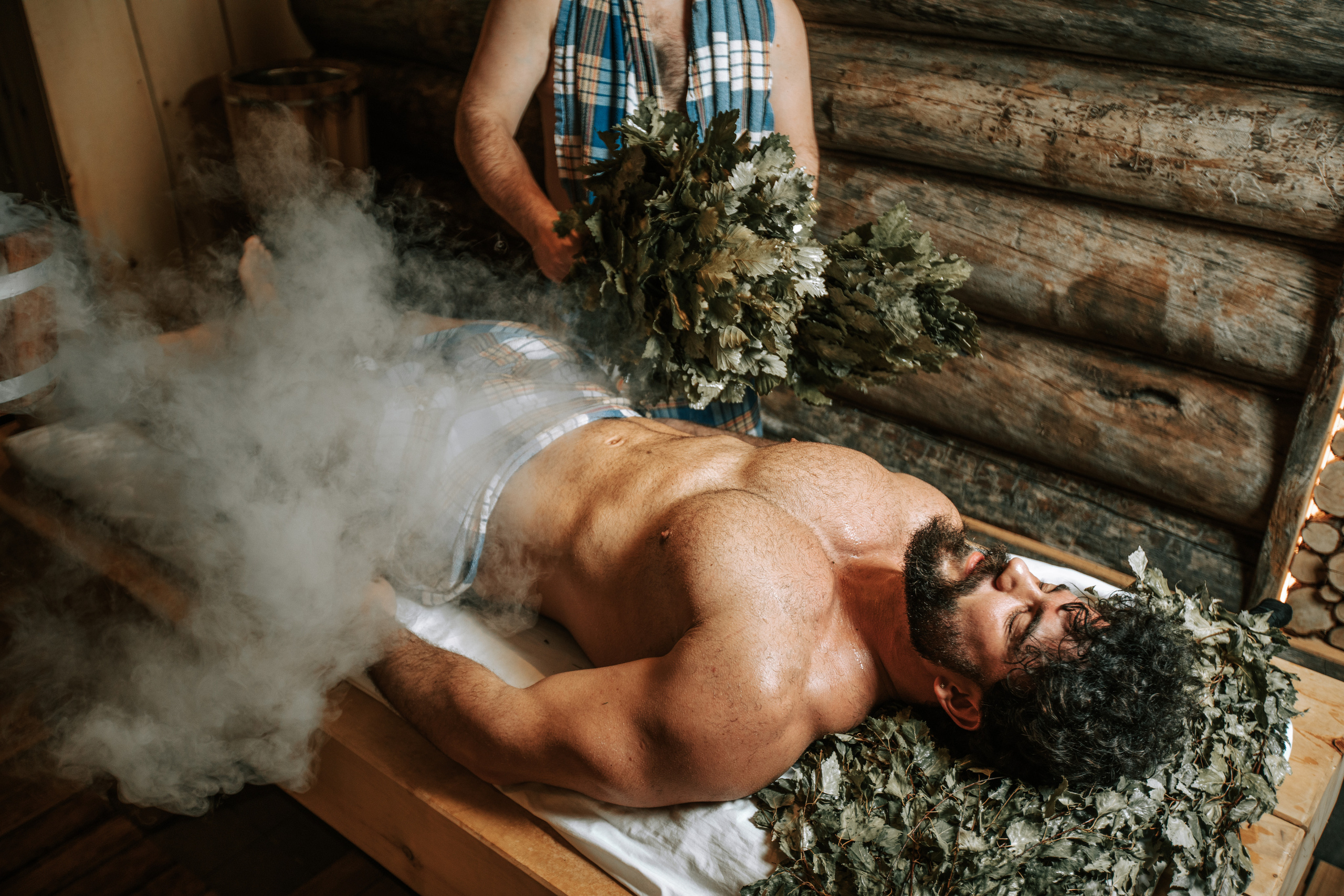 банщик парит веником мужчину в бане