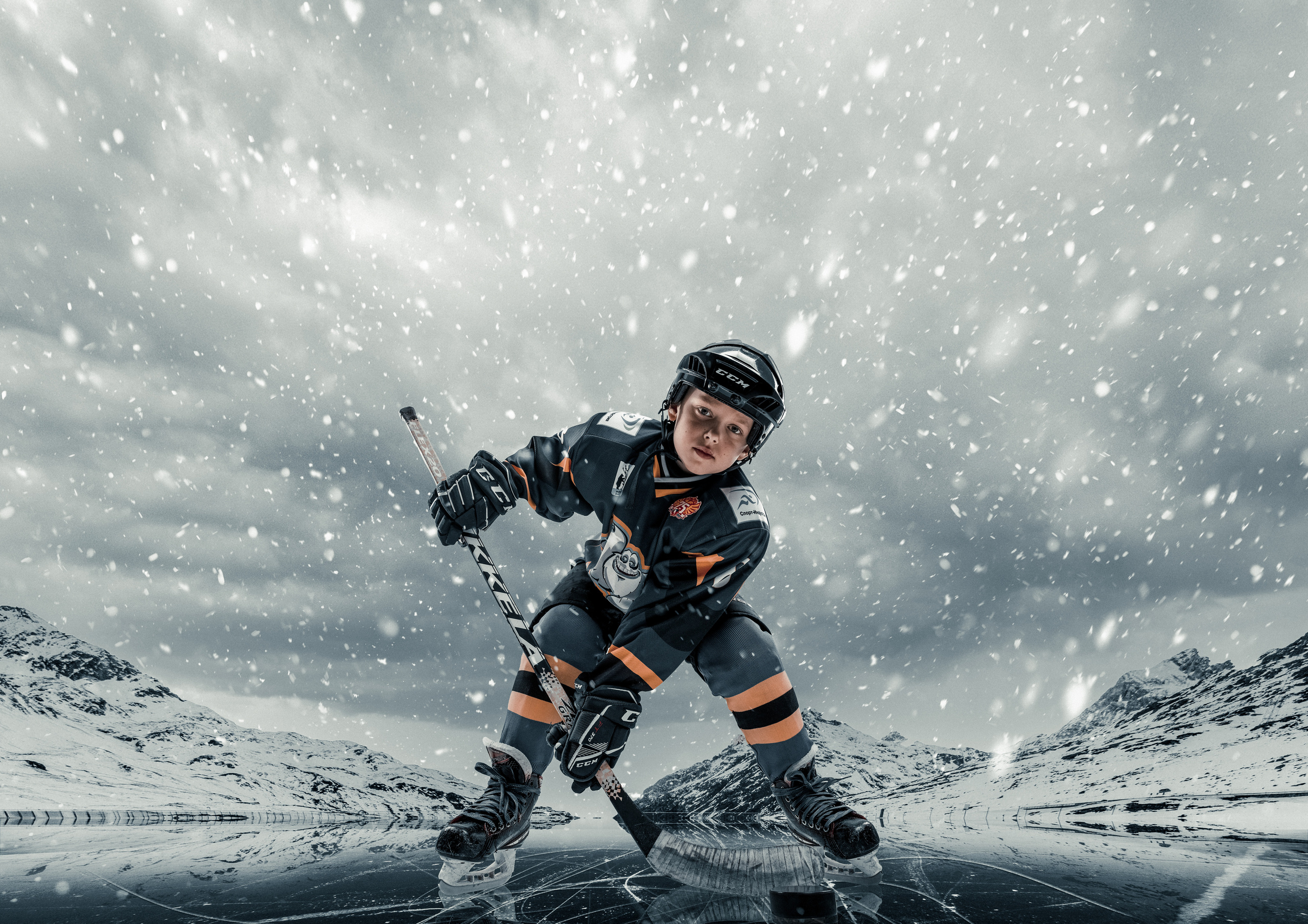 мальчик с клюшкой отбивает шайбу на фоне гор