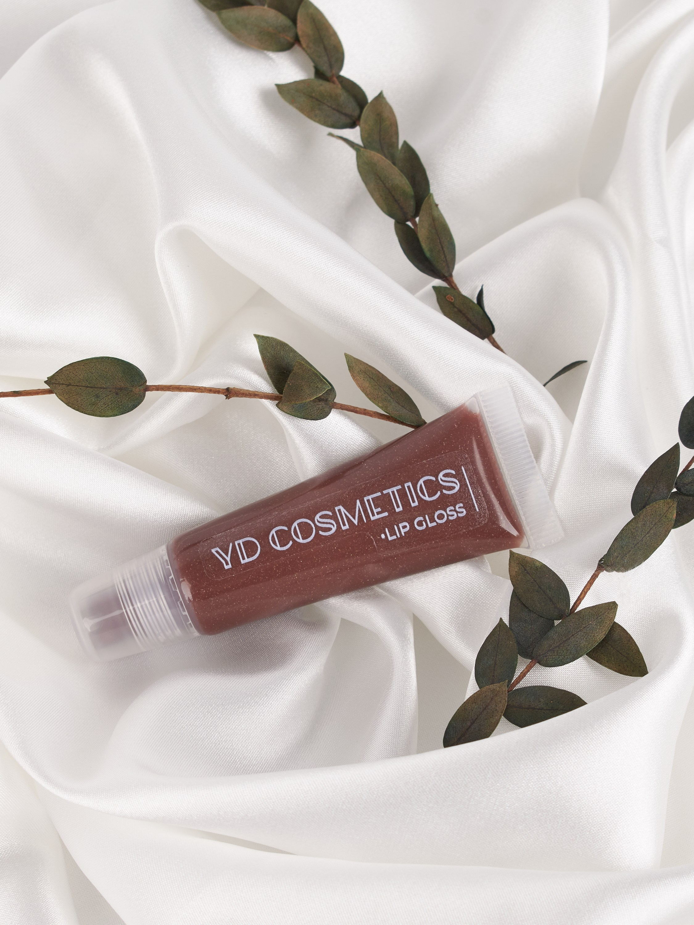 Коричневый блеск для губ на белой ткани с зелеными ветками