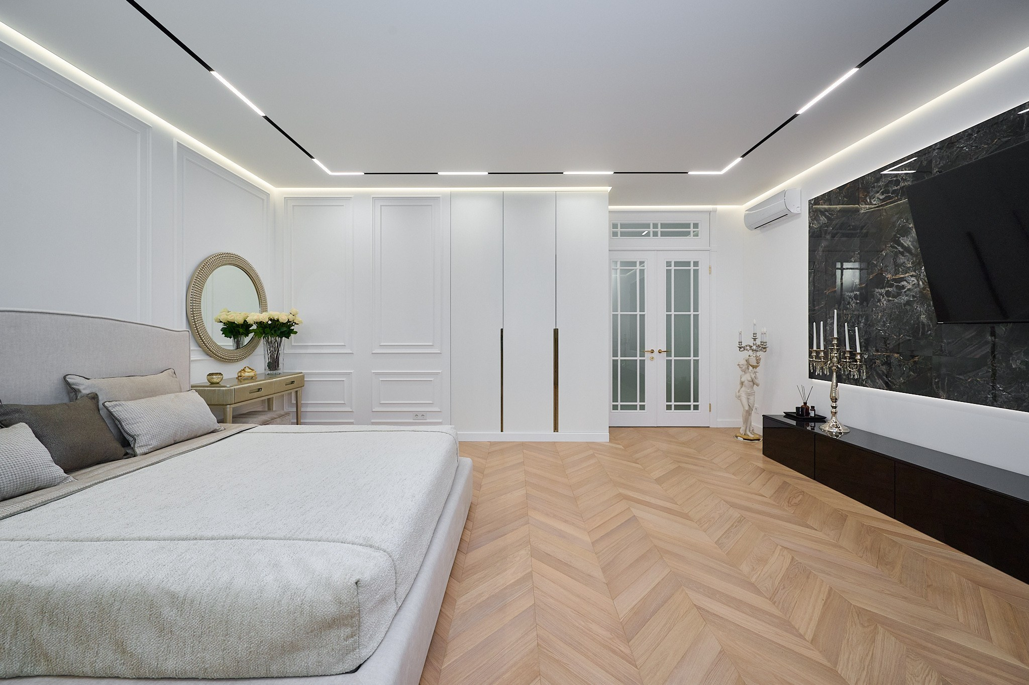 комната светлые оттенки белая кровать большой белый шкаф столик телевизор белые двери круглое зеркало 