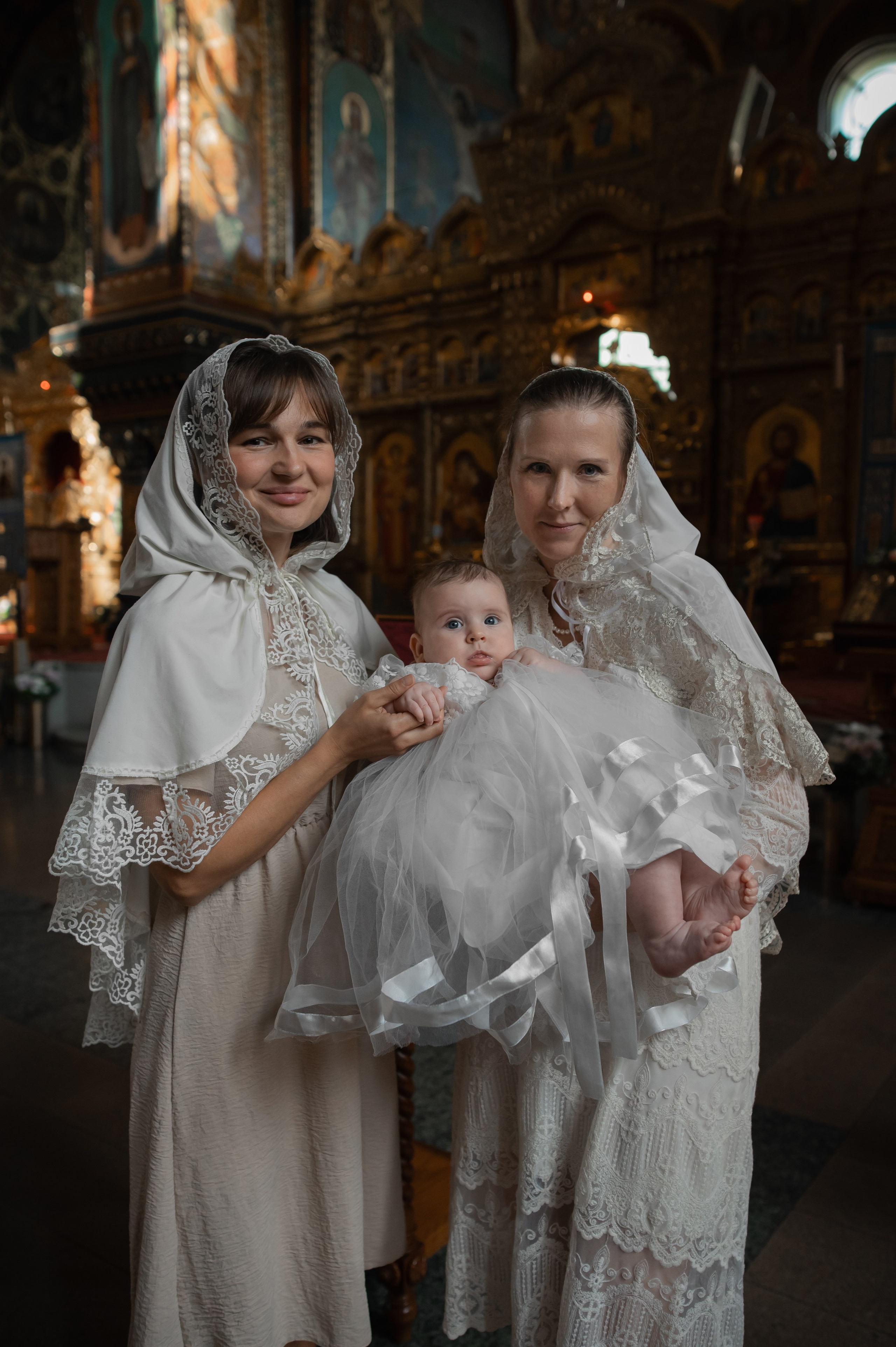 мама и крёстная держат малышку перед крещением в Оптинском подворье Санкт-Петербурга