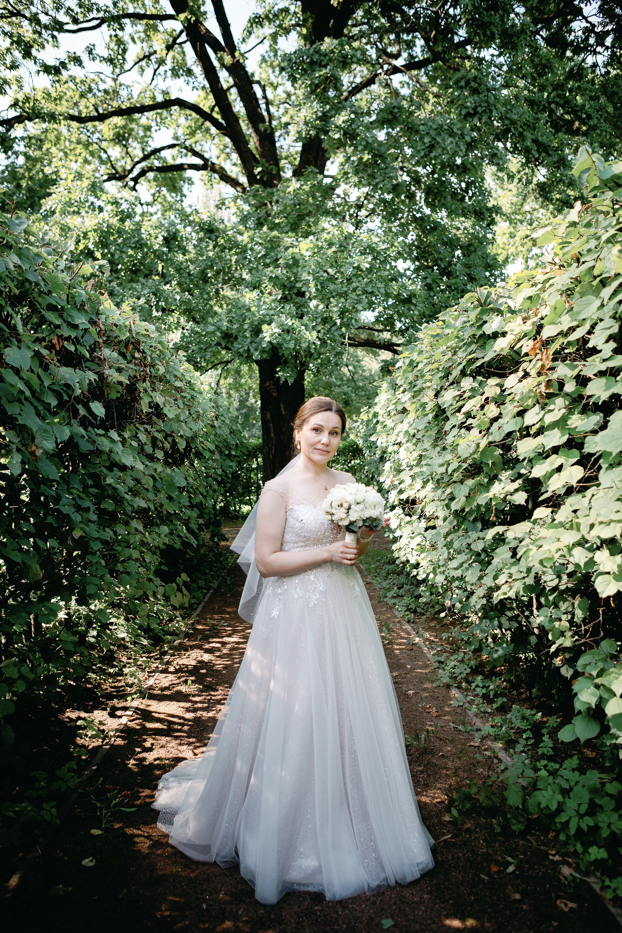 Невеста в свадебном платье стоит под деревом