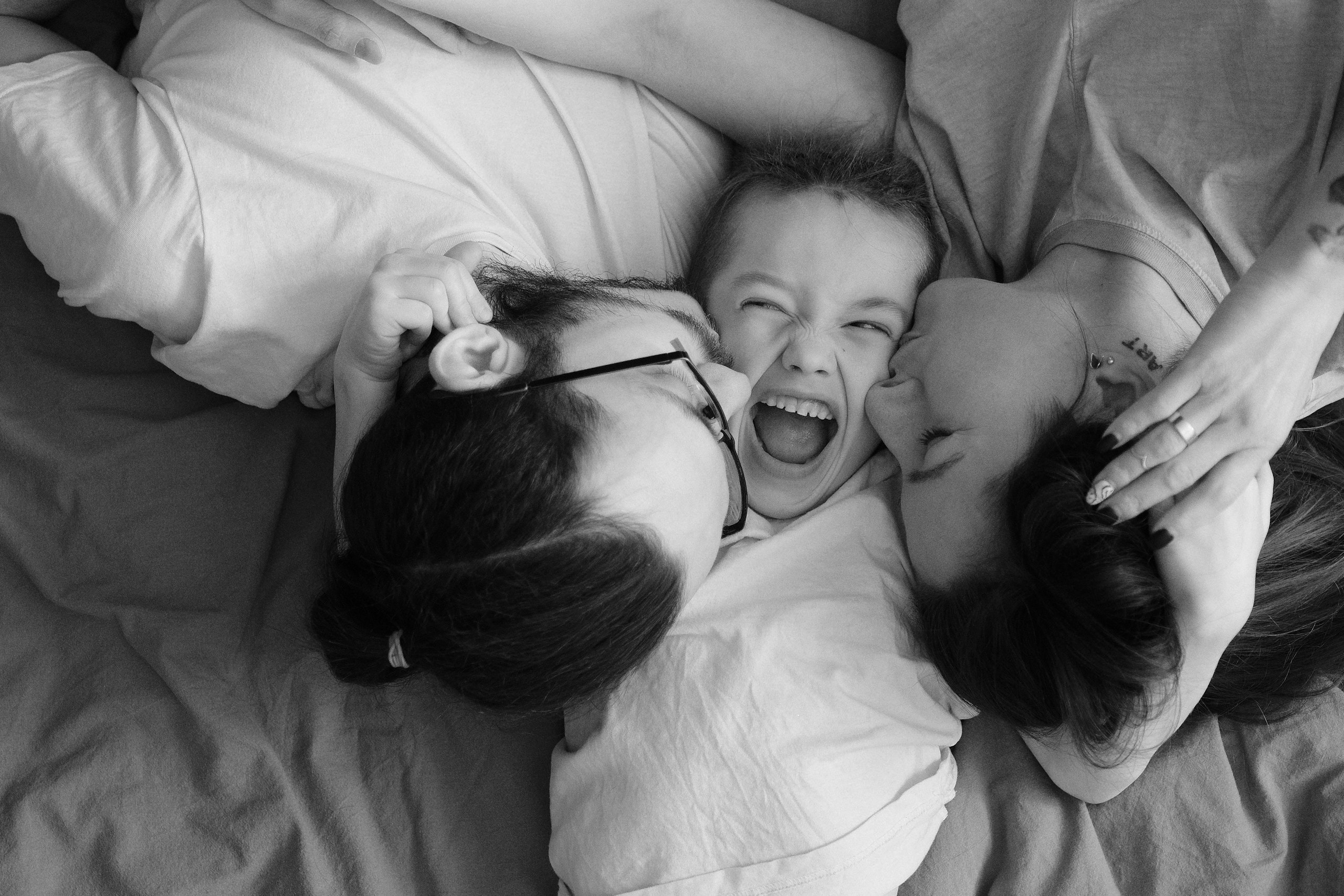 Счастливый мальчик обнимает своих родителей утром в постеле. Семейная фотосессия в Санкт-Петербурге