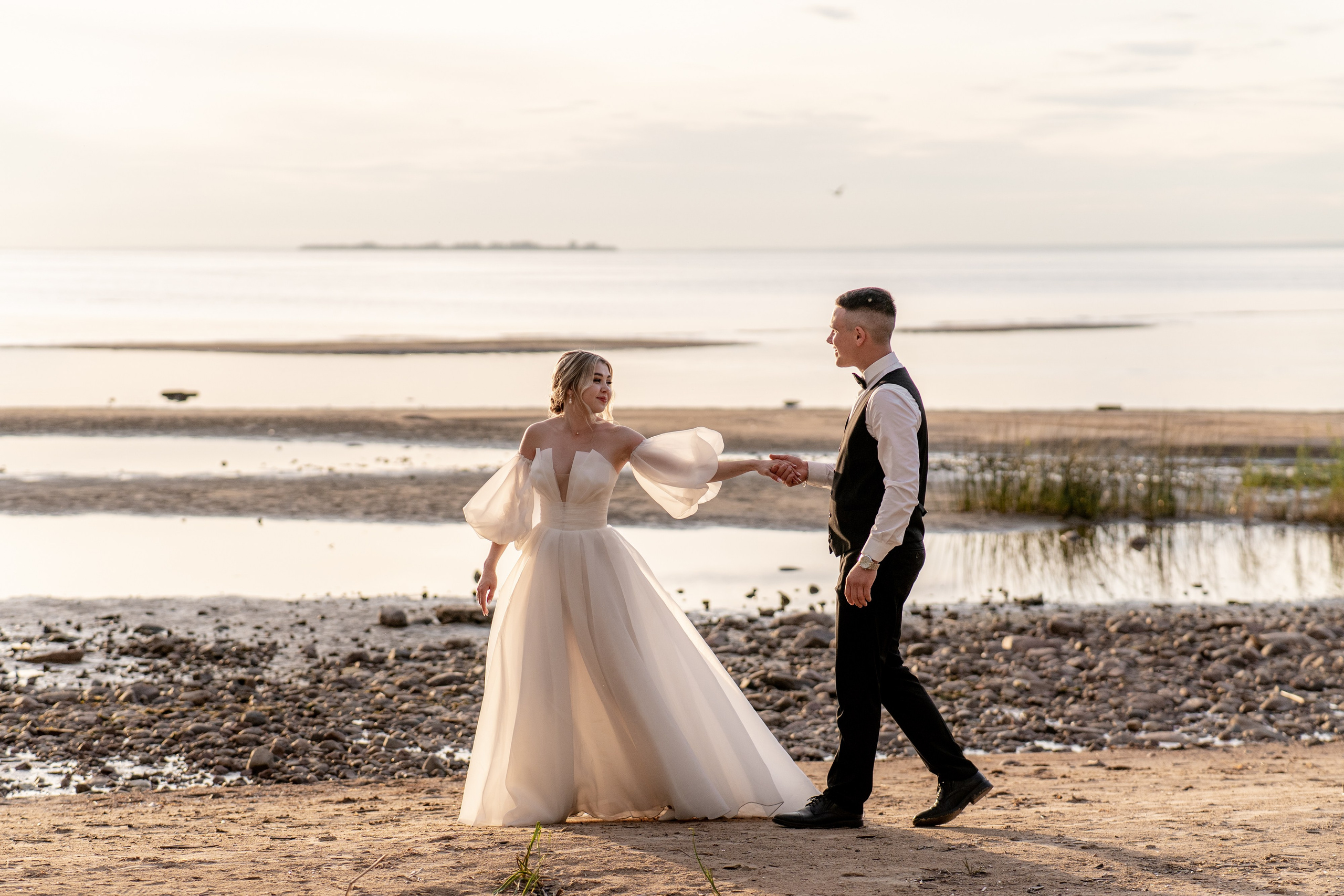 Жених и невеста идут у моря и заходящего солнца в Санкт-Петербурге на Финском заливе