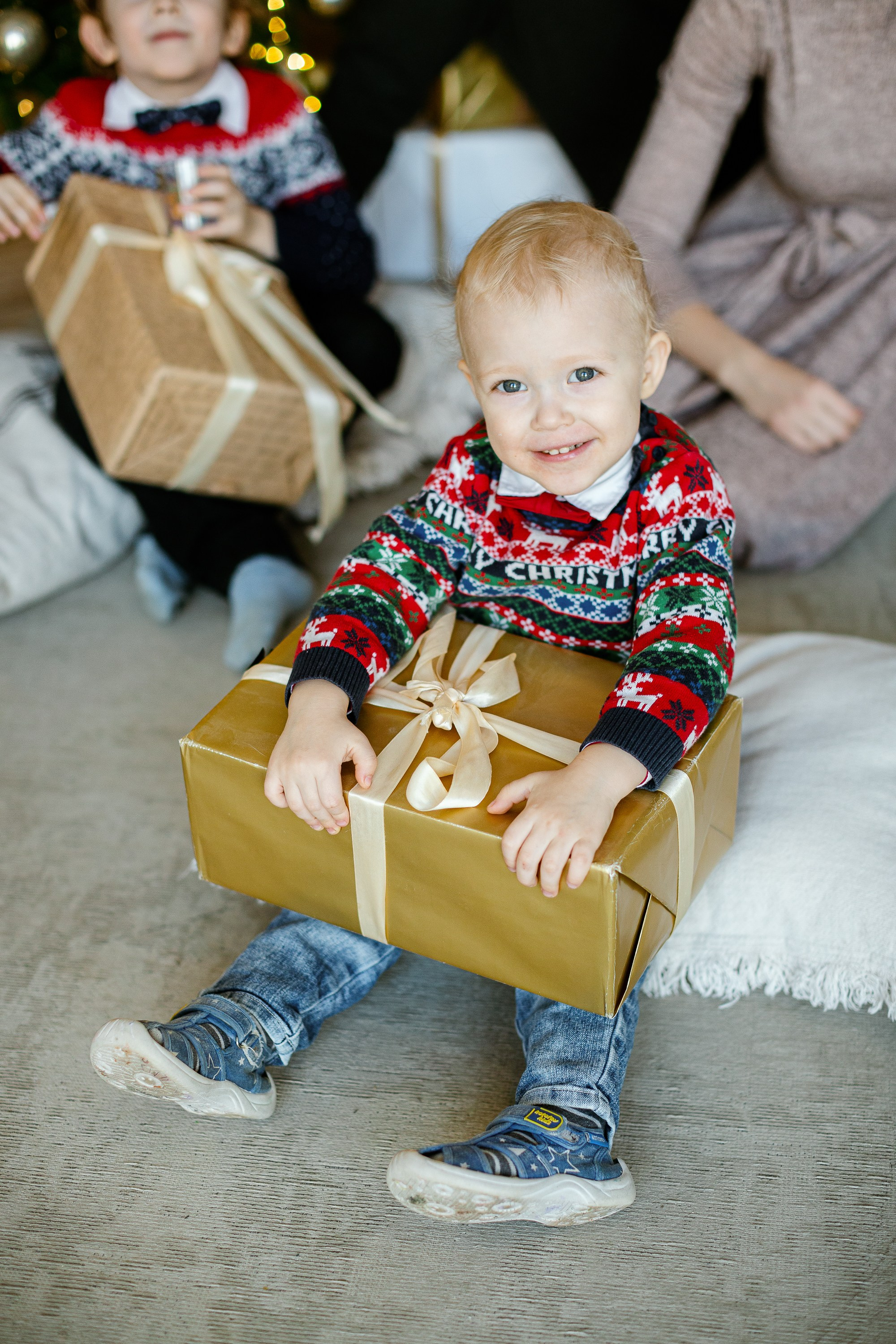 Малыш сидит на полу и держит в руках новогодний подарок.