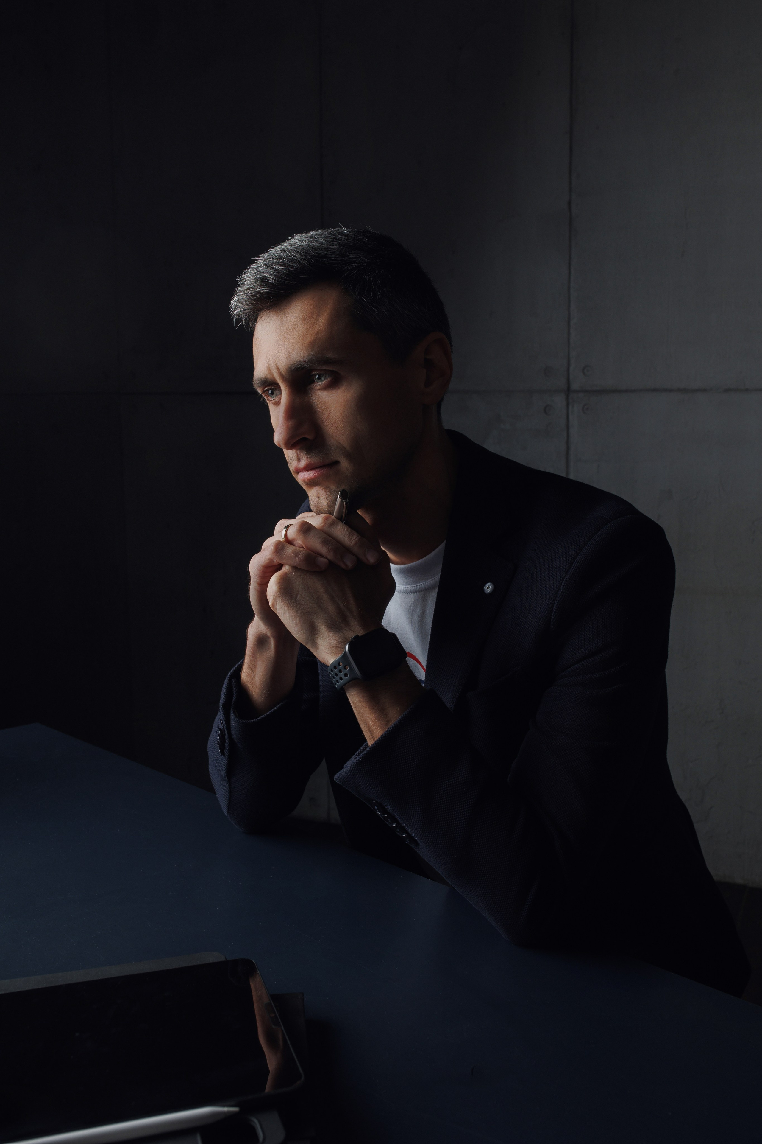 Момент размышления: бизнесмен в полутьме сидит за столом в глубокой задумчивости. Психологический портрет в деловой среде.