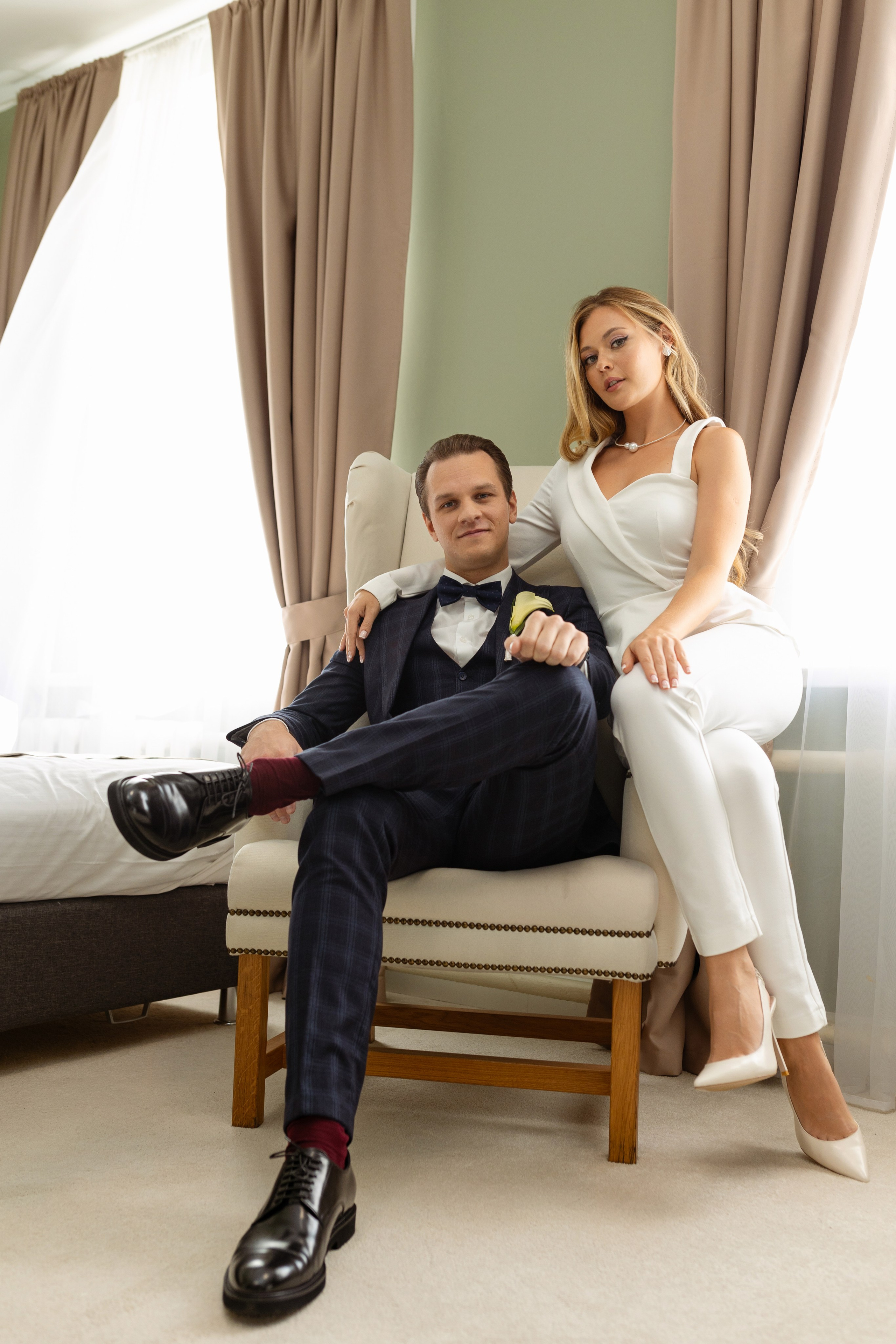 На кресле сидит жених, на подлокотнике сидит невеста.