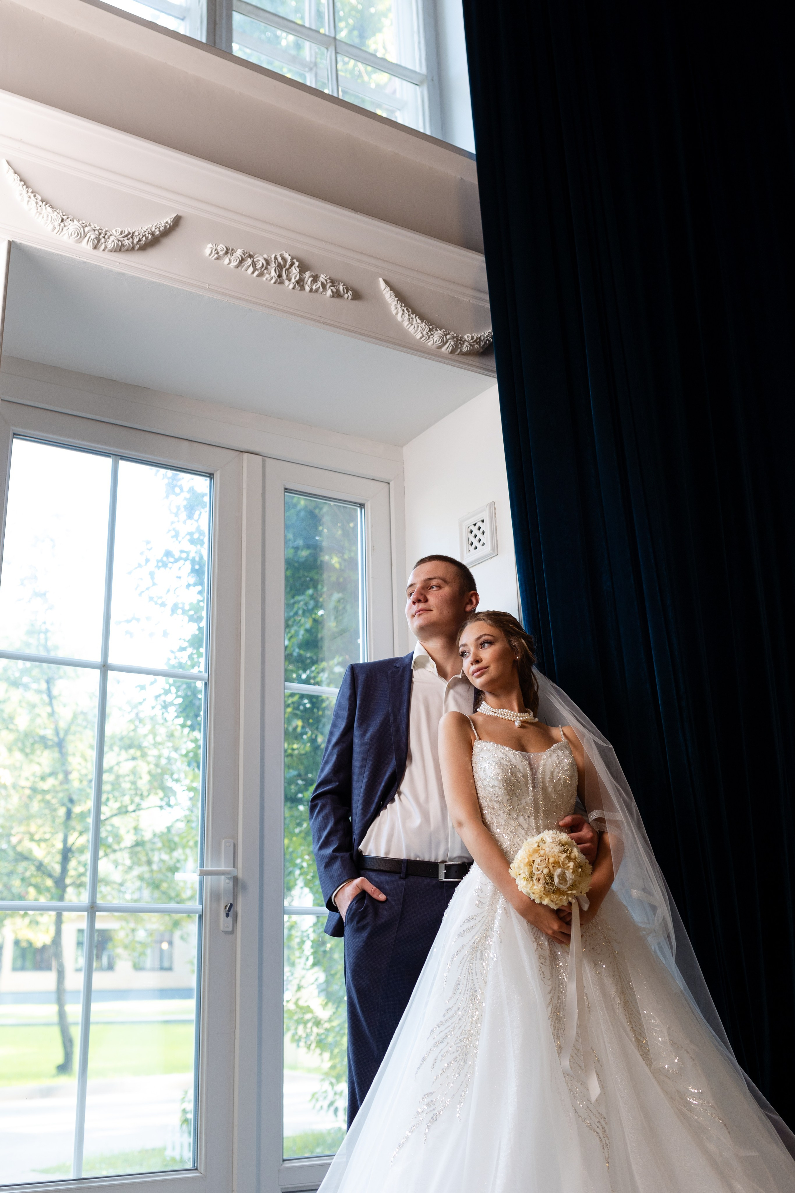 Молодые стоят у большого окна.