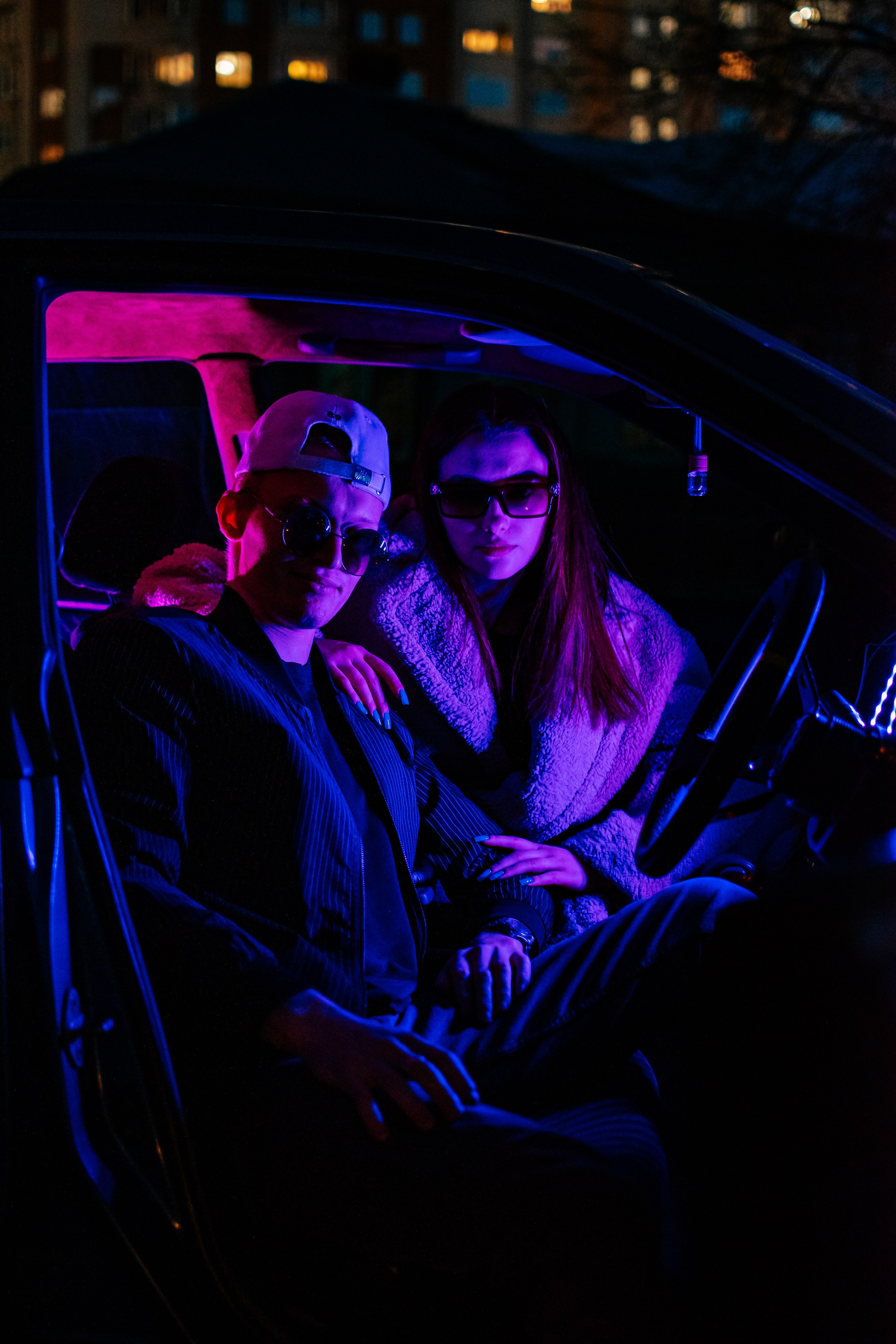 Парень и девушка сидят в машине, подсвеченные неоновым светом