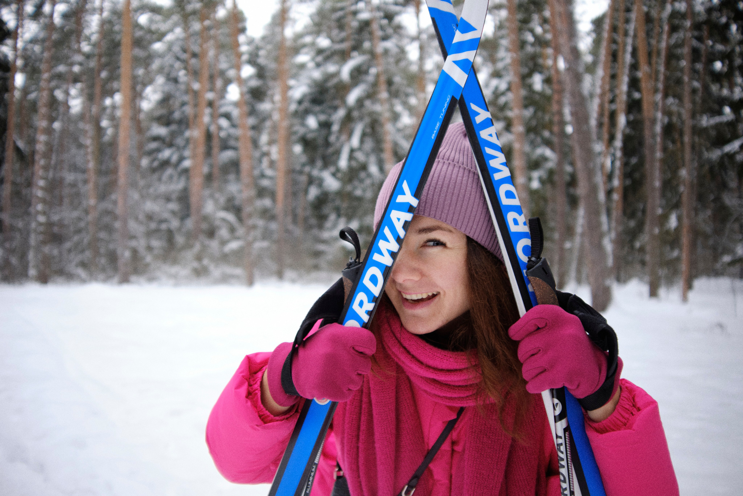 Женщина выглядывает из-под скрещенных лыж на фоне зимнего леса