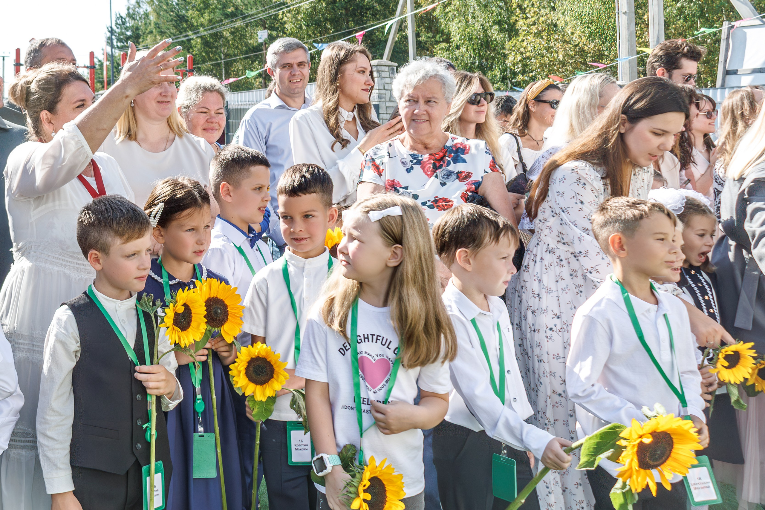 Линейка 1 сентября в школе - дети с букетами, радостные родители и учителя; дети обнимаются, радуются встрече с друзьями после каникул