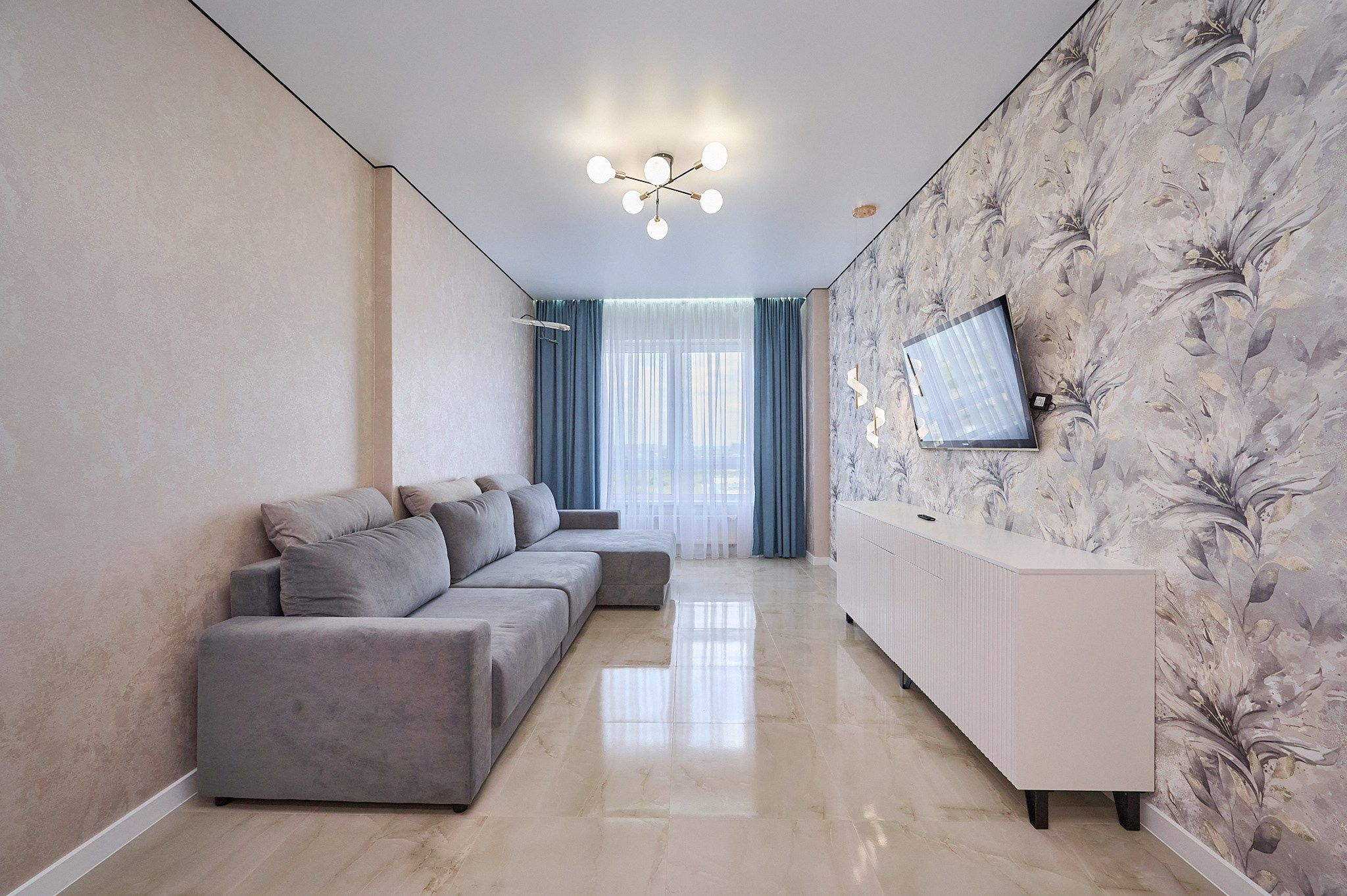 гостиная светлых тонов серый диван белый комод телевизор голубые шторы одна стена цветная