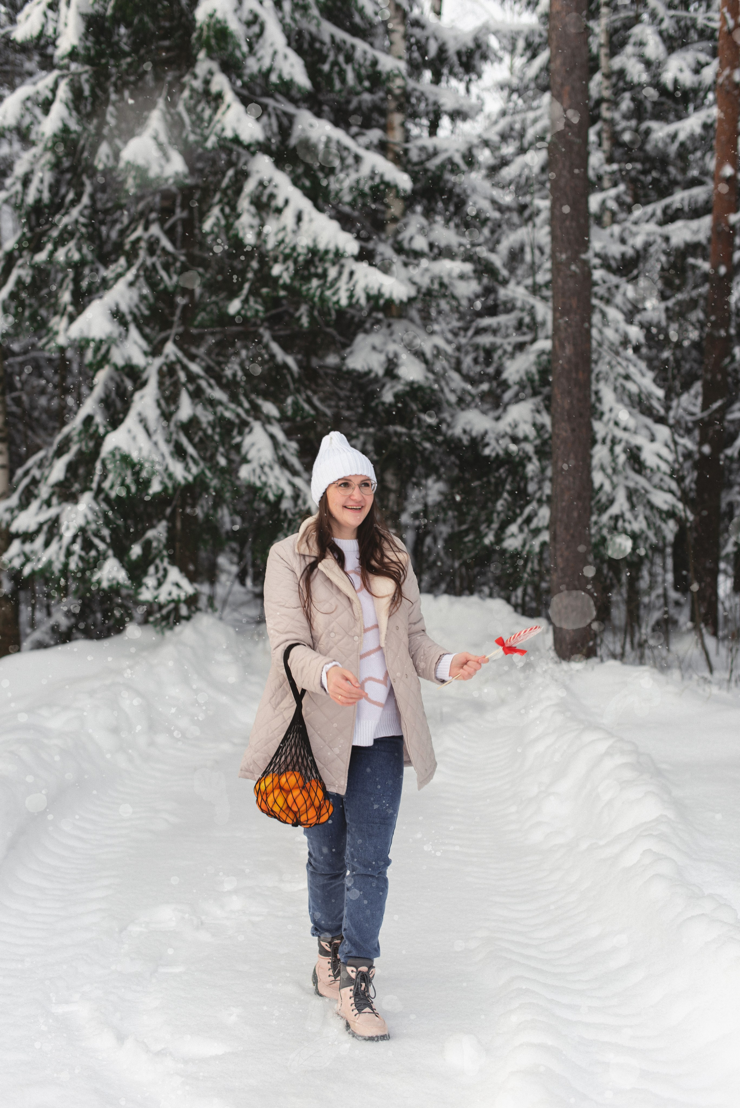 Зимняя сцена: девушка играет с мандаринами в сетке, на фоне лесная местность.