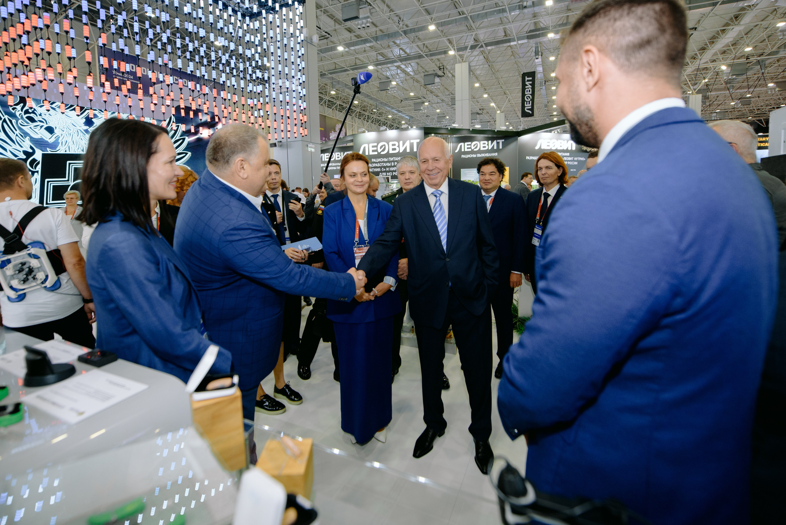 Фотография с выставки, на которой изображены участники, обсуждающие экспонаты.  Фотография репортажного характера, запечатлевшая важный момент корпоративного мероприятия. Министр обороны РФ Белоусов. Чемезов Роснано. Армия 2024. Вероника Скворцова