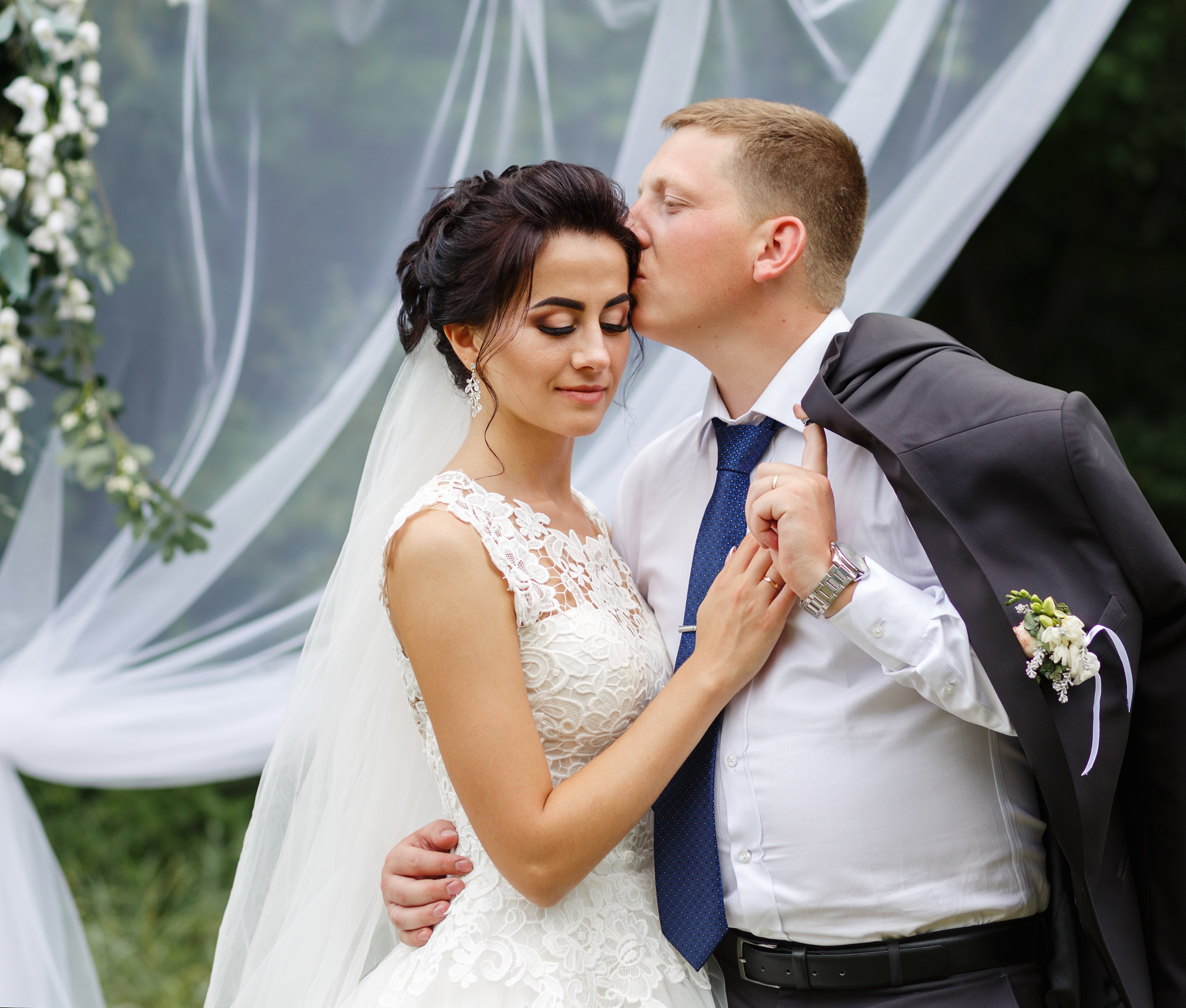 жених целует невесту в висок и обнимает ее за талию. одетый в синих костюм