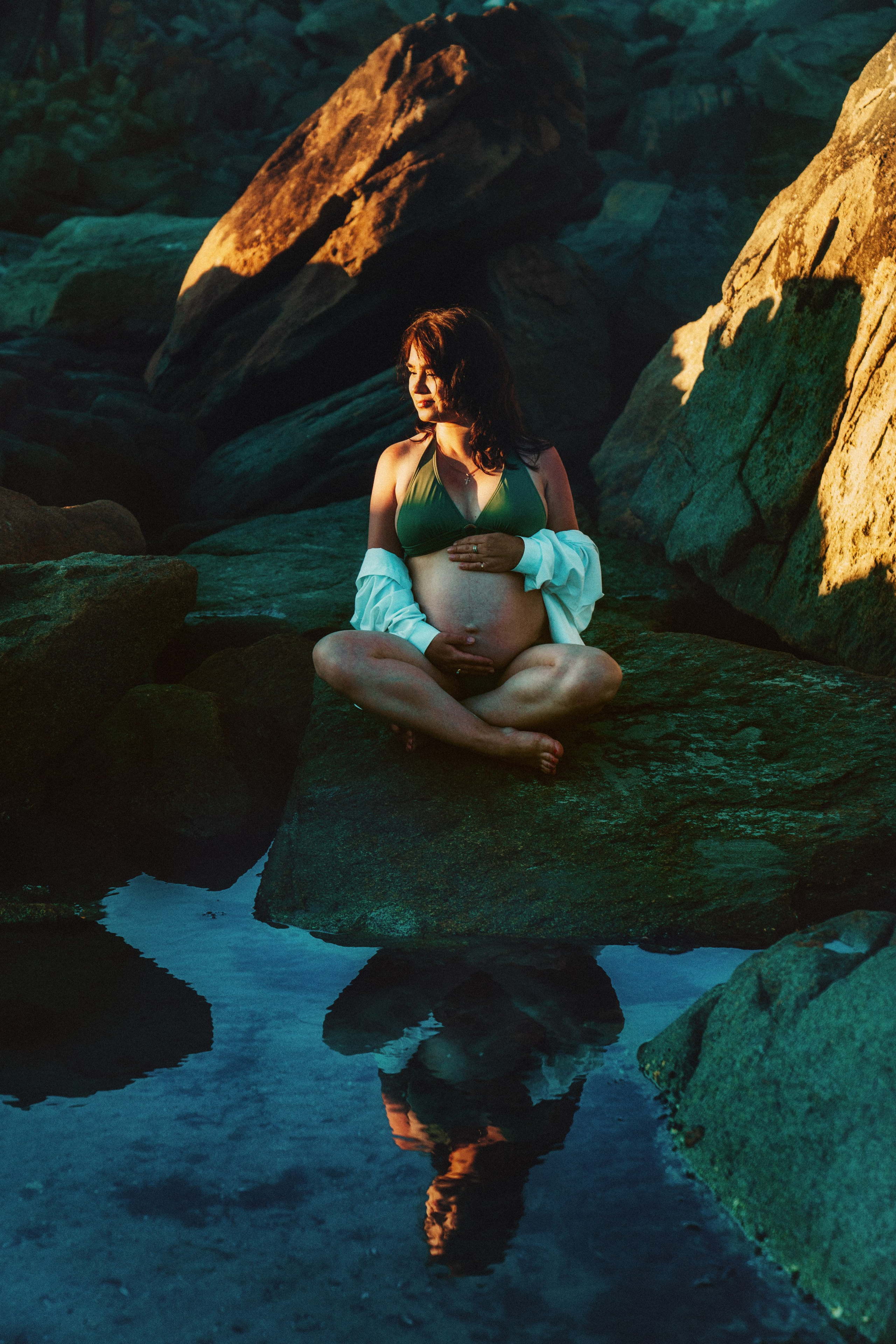 Беременная девушка сидит на камнях. Отражение девушки в воде