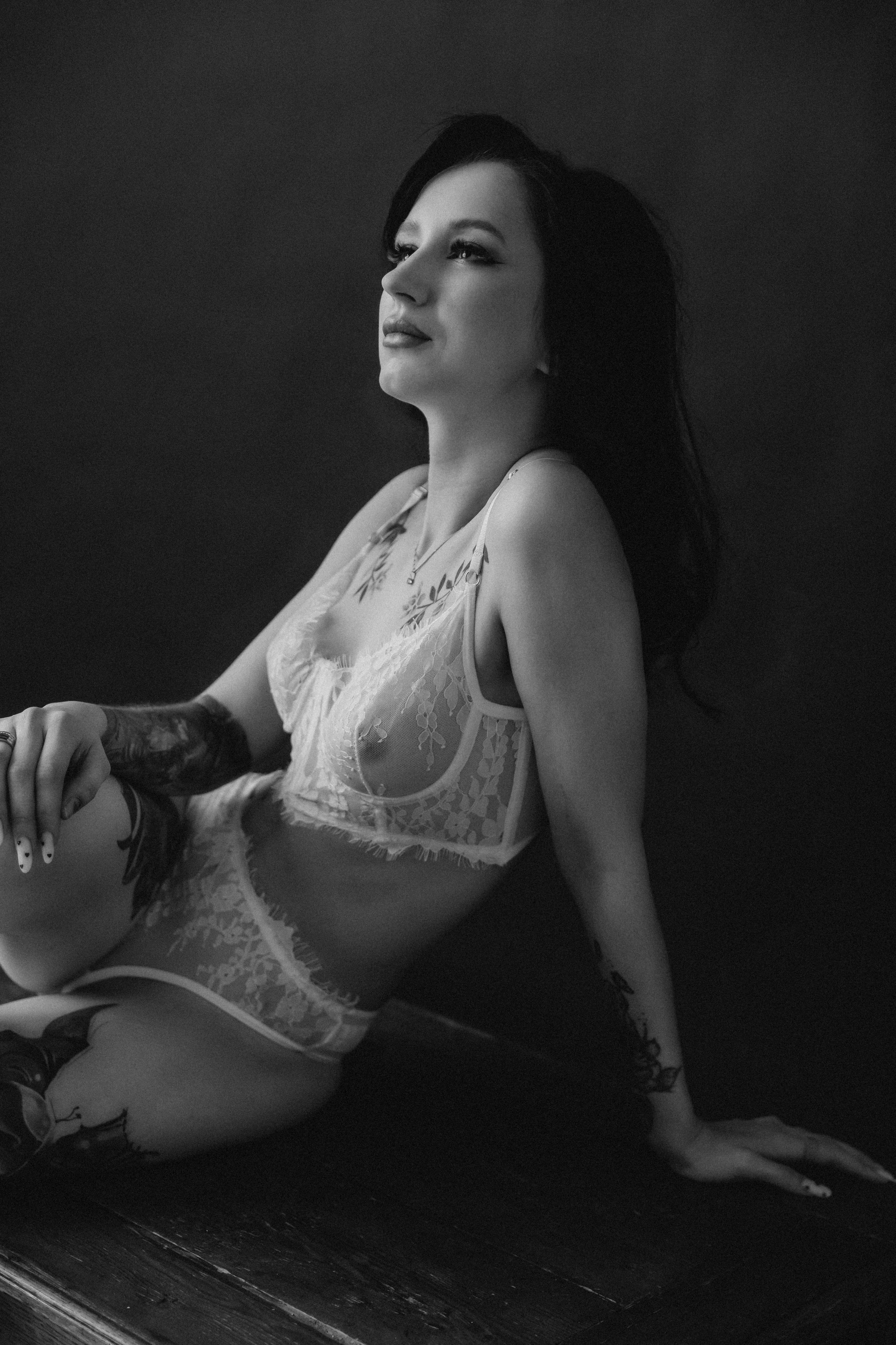 Женщина в кружевном белье сидит на кровати, мягкий естественный свет падает из окна.