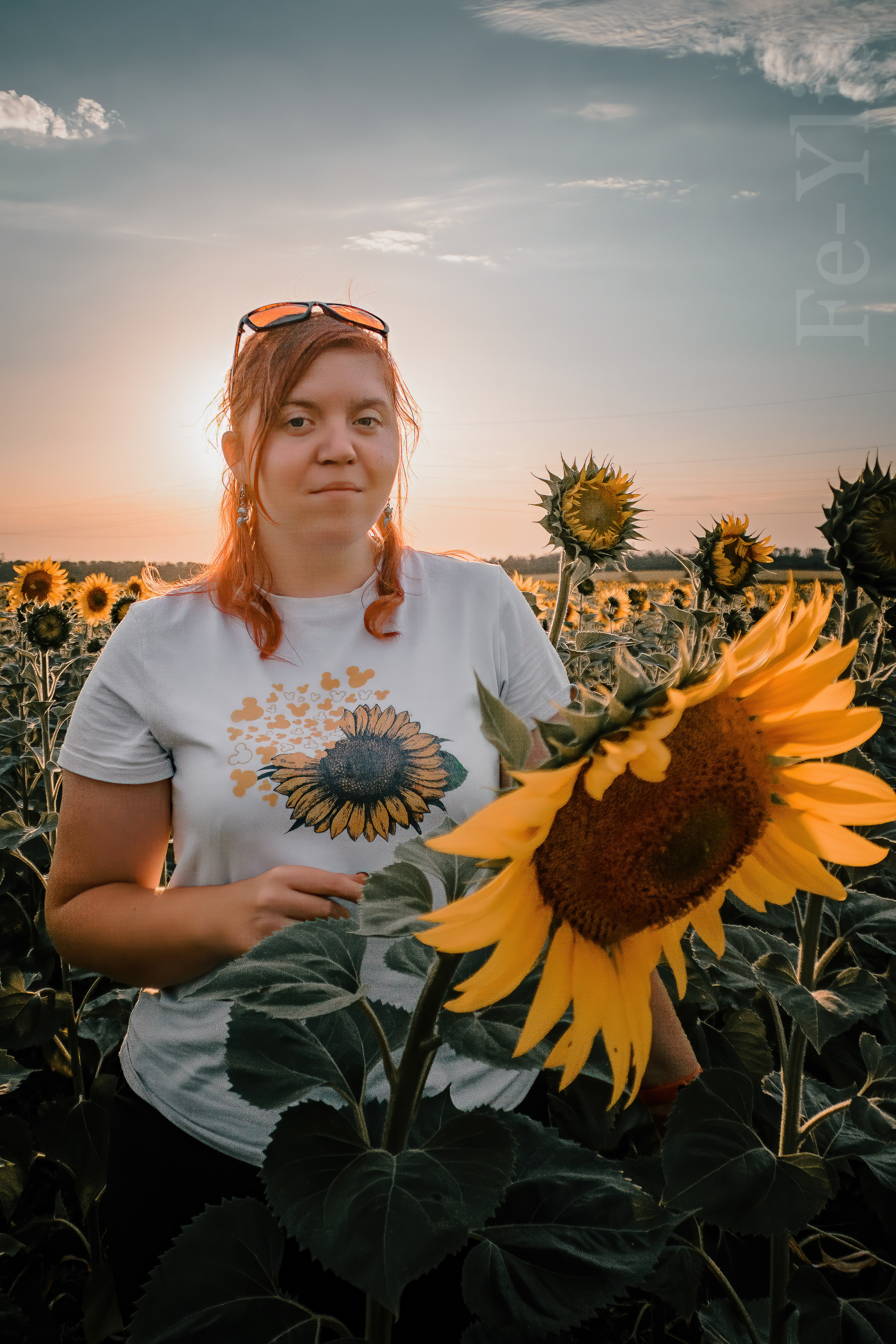 На девушке футболка с подсолнухом, а перед ней настоящий подсолнух