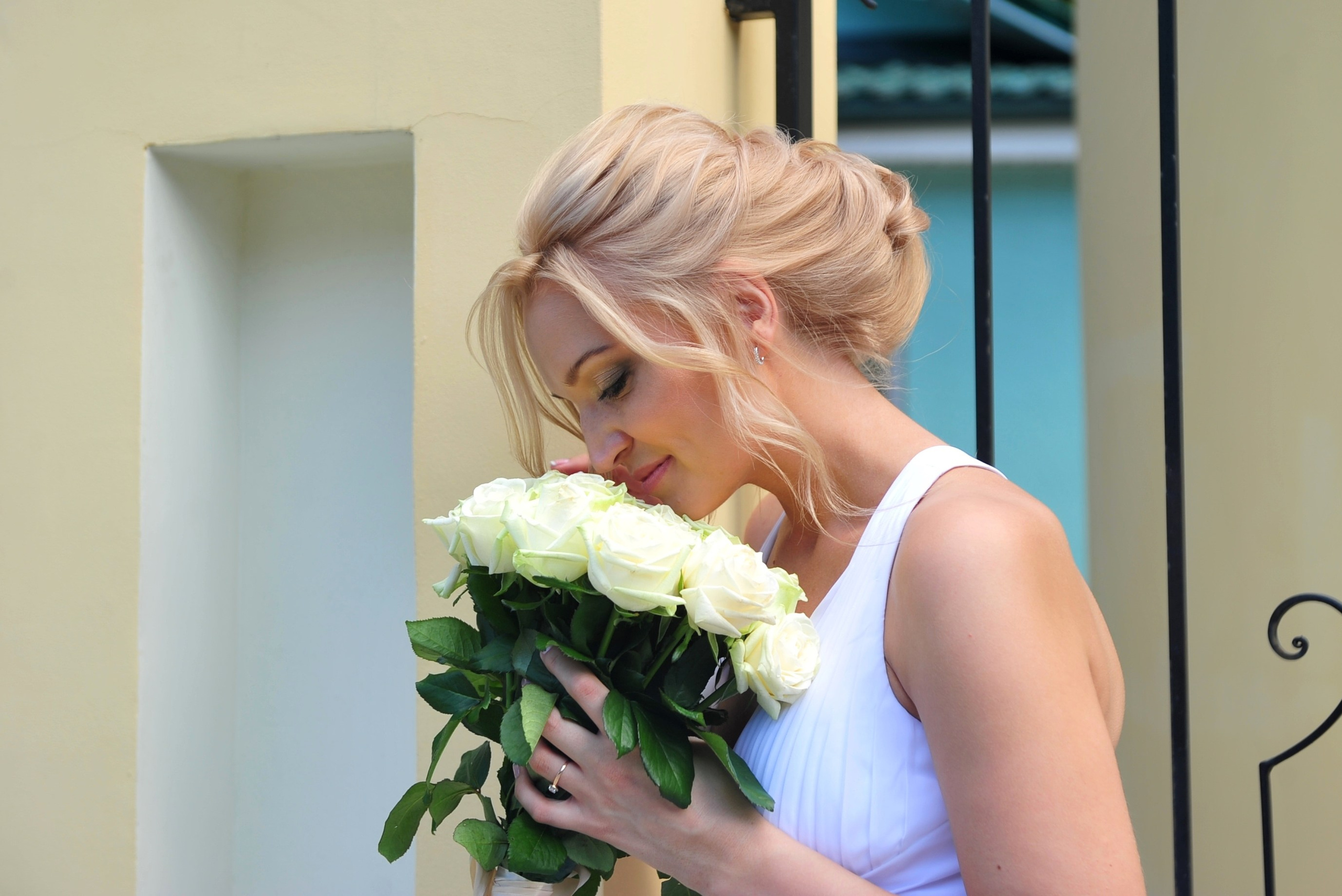 Свадьба на Воробьёвых Горах рядом с МГУ, невеста нюхает букет из кремовых роз на фоне желтой каменной церковной ограды и кованной решетки