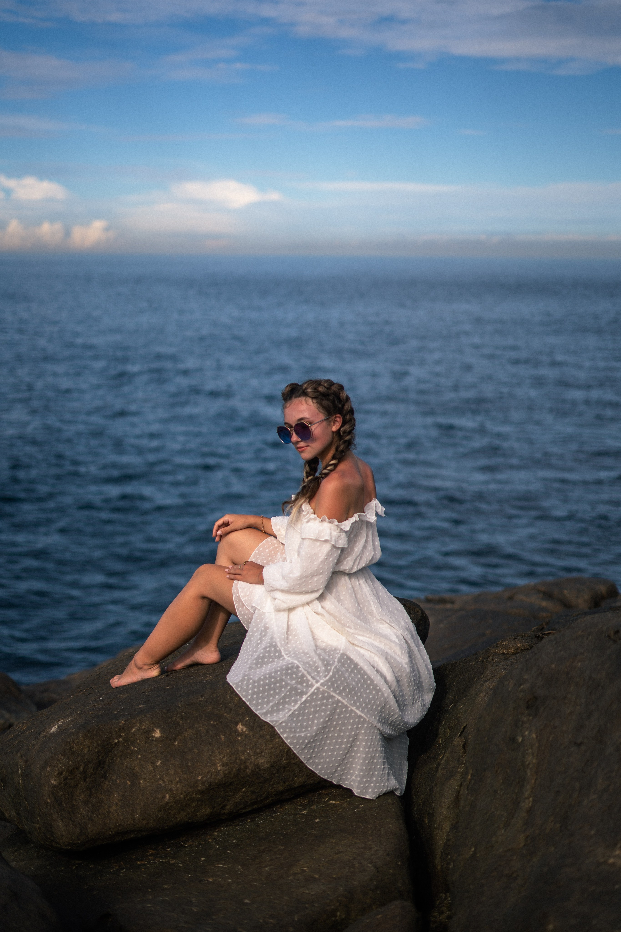 a girl in a white dress and glasses with an ocean view at sunset