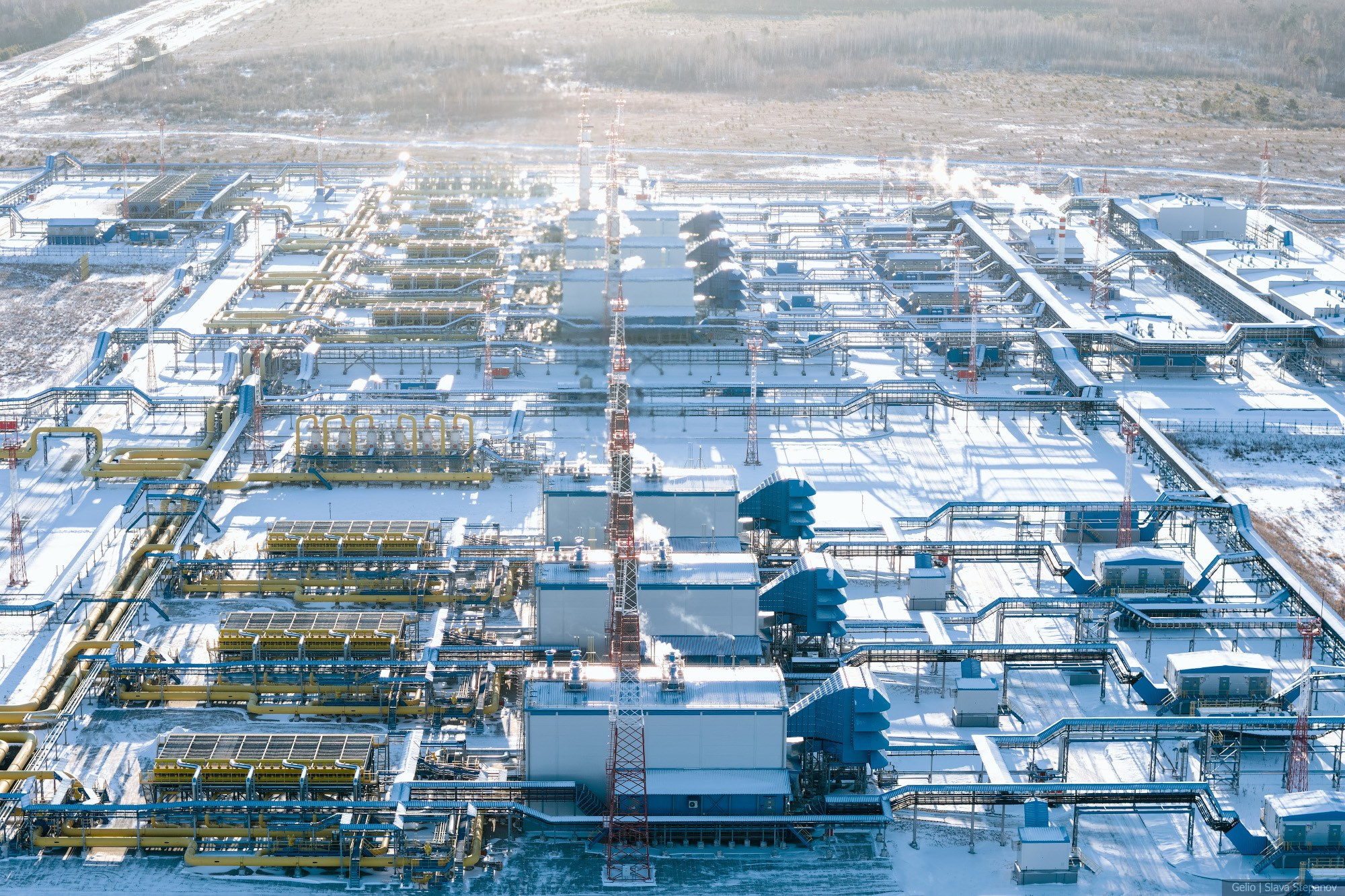 Заснеженная территория современной газокомпрессорной станции, чёткие ряды производственных цехов с мощными вентиляторами морозным днём с высоты птичьего полёта, Gelio.